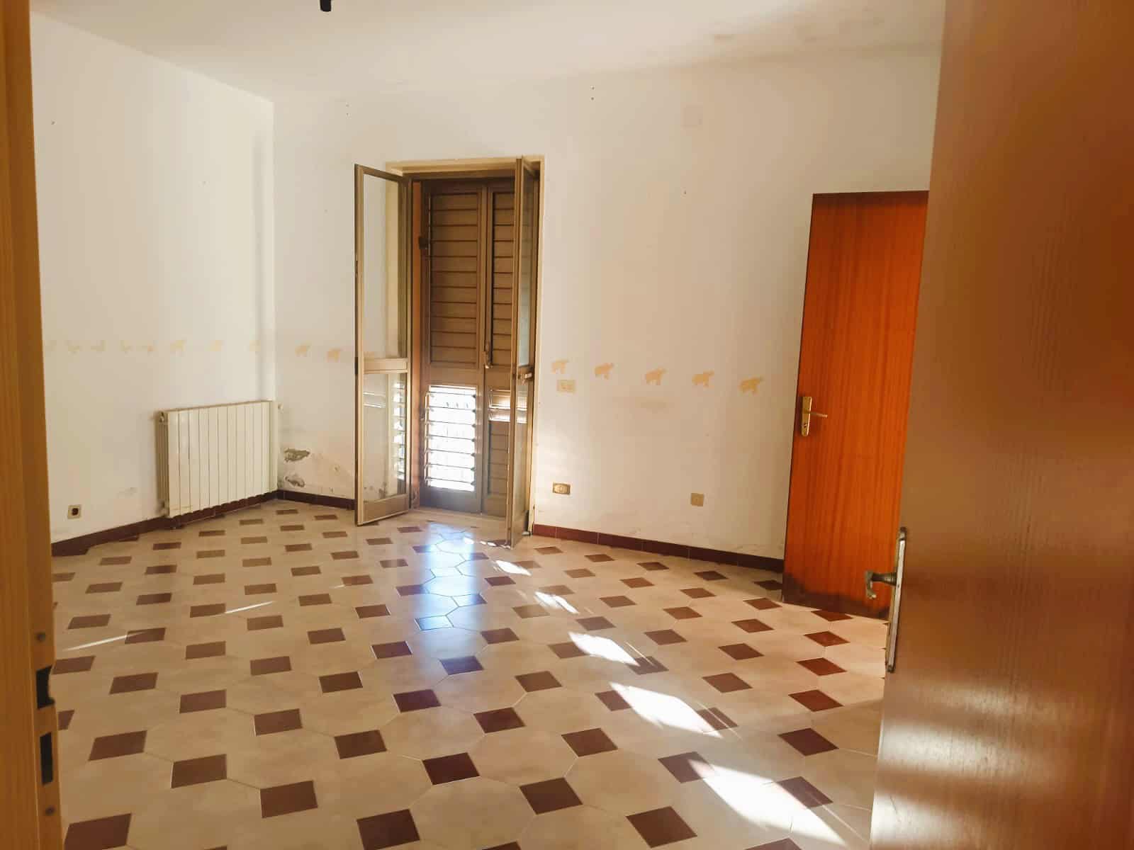 Interno di stanza vuota con pavimento in piastrelle, pareti bianche con decorazioni animalier, finestra con persiane e porta in legno, nessun arredamento, luce naturale; ideale per appartamento o casa in vendita o affitto.