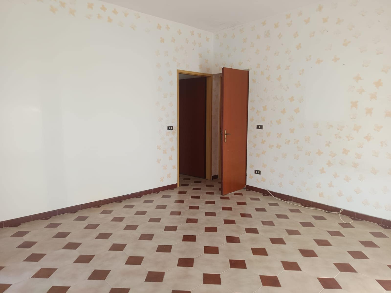 Porta e pareti di una stanza vuota con rivestimento a mosaico di piastrelle beige e marroni, ambiente luminoso, ideale per arredare una casa o appartamento.