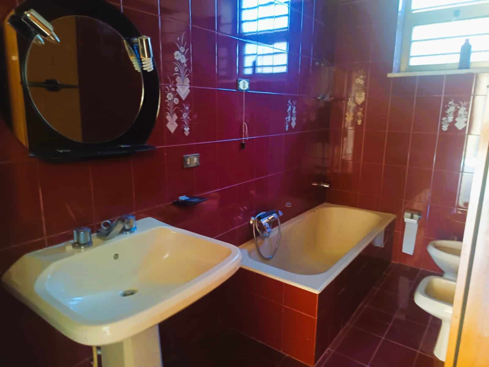 Lavabo e vasca da bagno in bagno con pareti e pavimento in piastrelle rosse con motivo floreale. Finestra con grate per ventilazione naturale e altri accessori bagno.