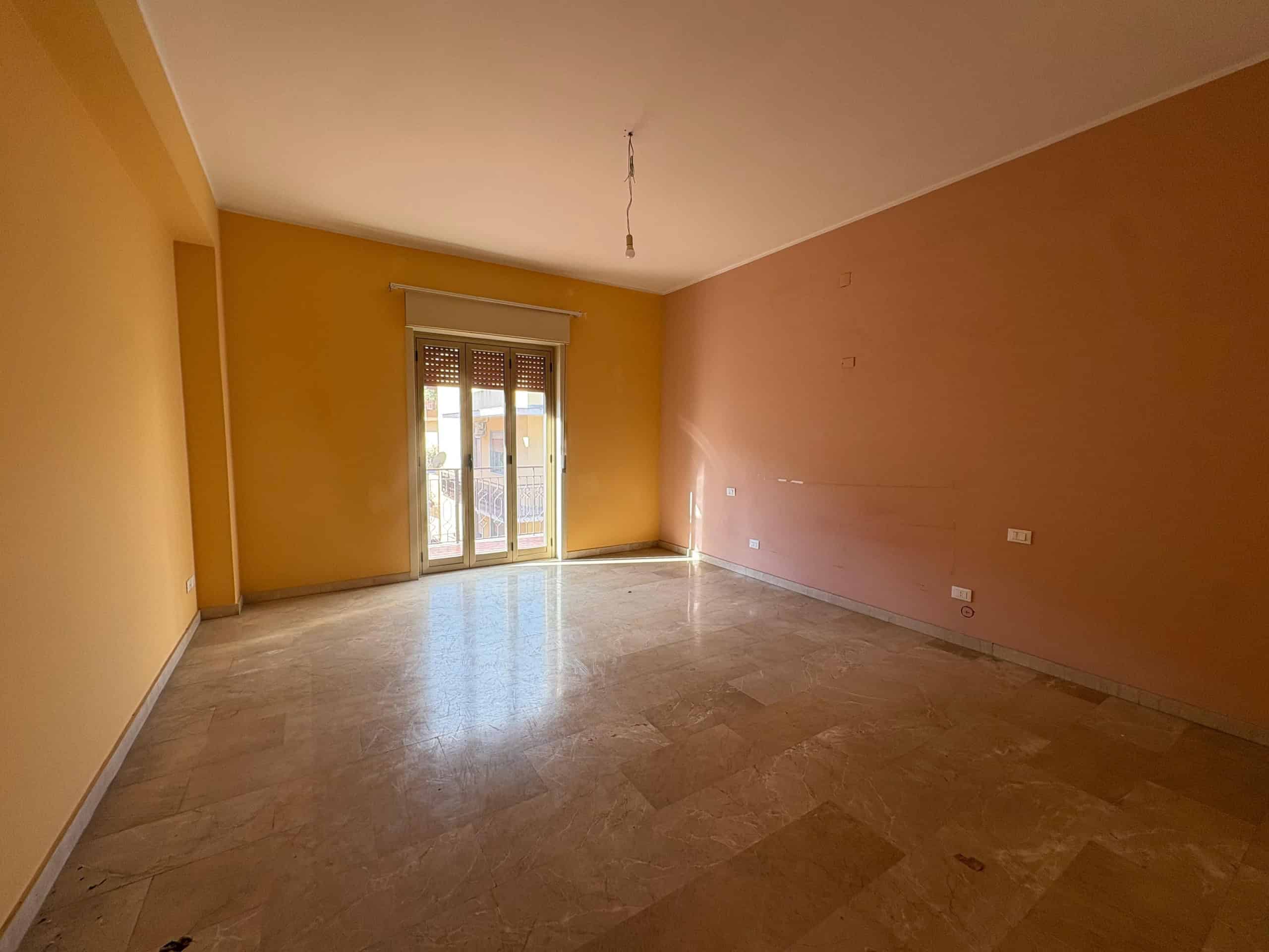 Ampio soggiorno luminoso con pareti color pesca, pavimento in marmo e accesso a balcone; ambiente ideale per abitazione o investimento immobiliare.