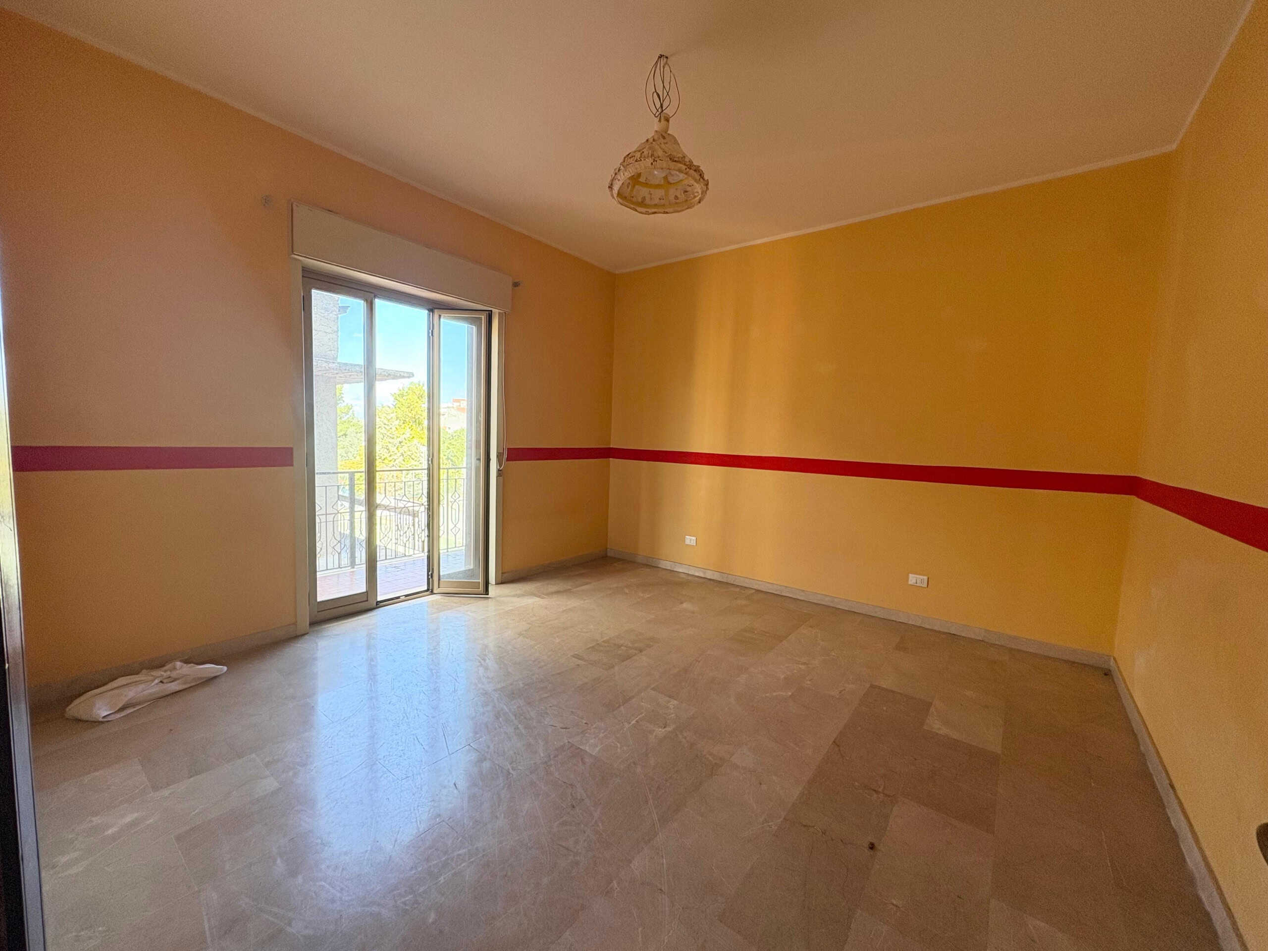 Spazioso soggiorno con pareti gialle, finestra a doppia anta che dà accesso a un balcone, pavimento in marmo e illuminazione naturale, ideale per la vendita o affitto di case di prestigio.