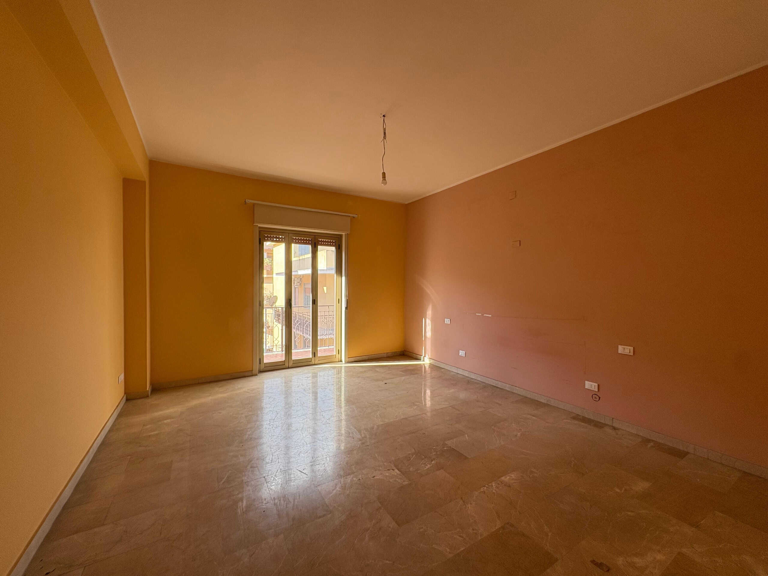 Ampio soggiorno vuoto con pareti color terracotta e luce naturale, ideale per appartamento in vendita o affitto a NextCasa, zona residenziale in Italia.