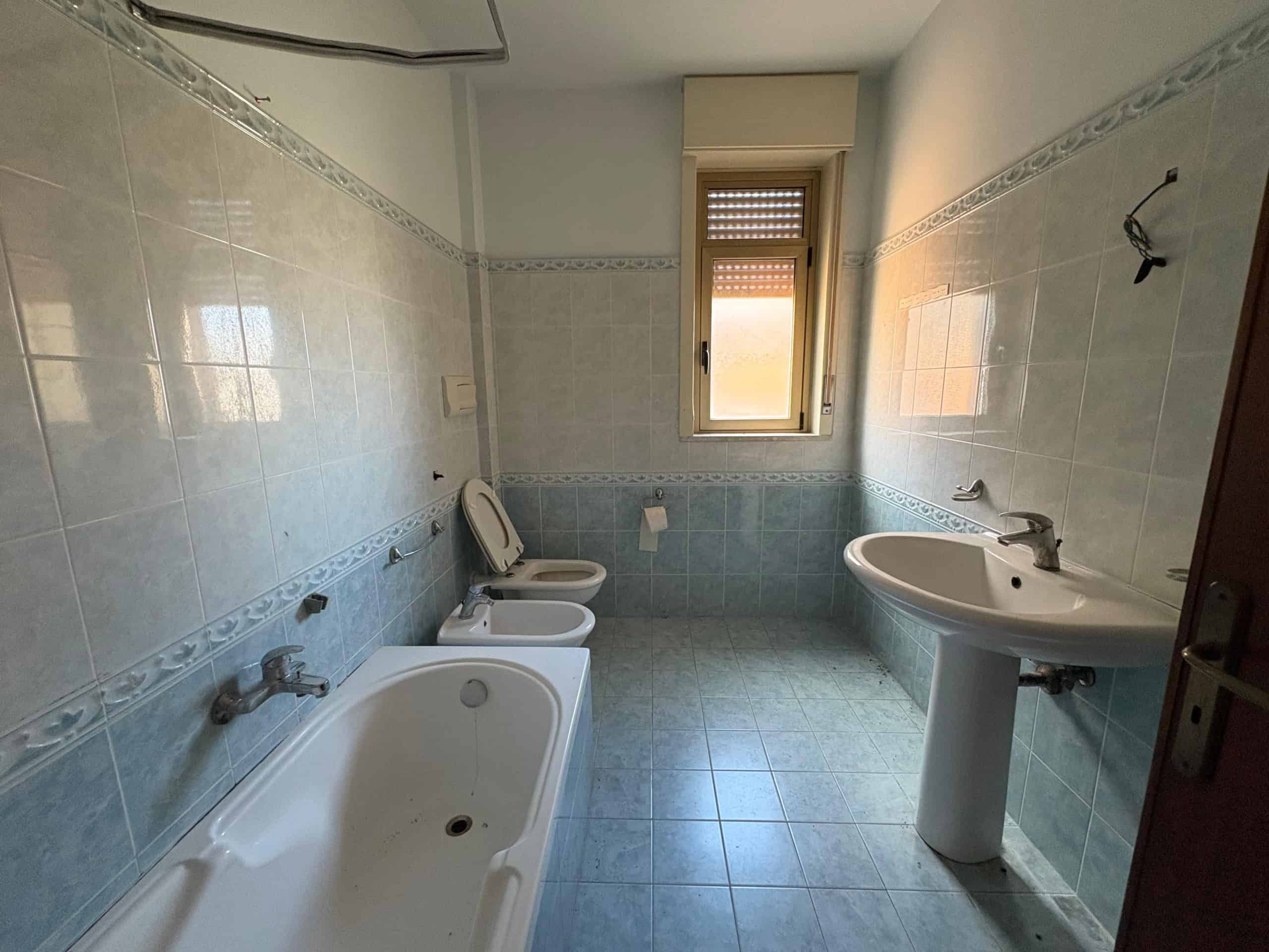 Bagno spazioso con accesso naturale alla luce, piastrelle blu e arredo semplice, ideale per residenze a Napoli e provincia, con servizi di ristrutturazione e progettazione edilizia.