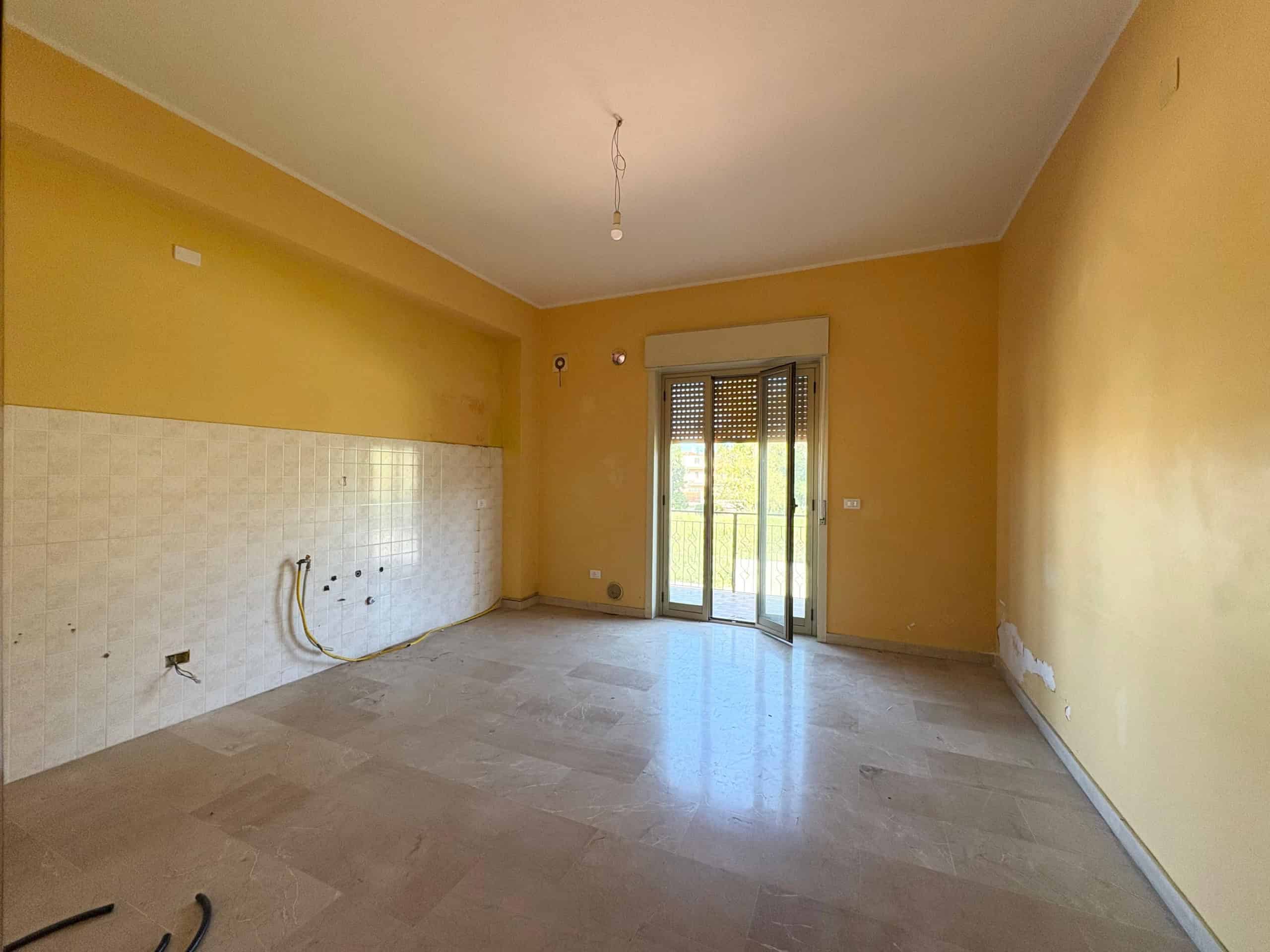 Spazio soggiorno vuoto in appartamento in fase di ristrutturazione con pareti gialle, terrazza e illuminazione naturale, ideale per ristrutturare e personalizzare la zona living.