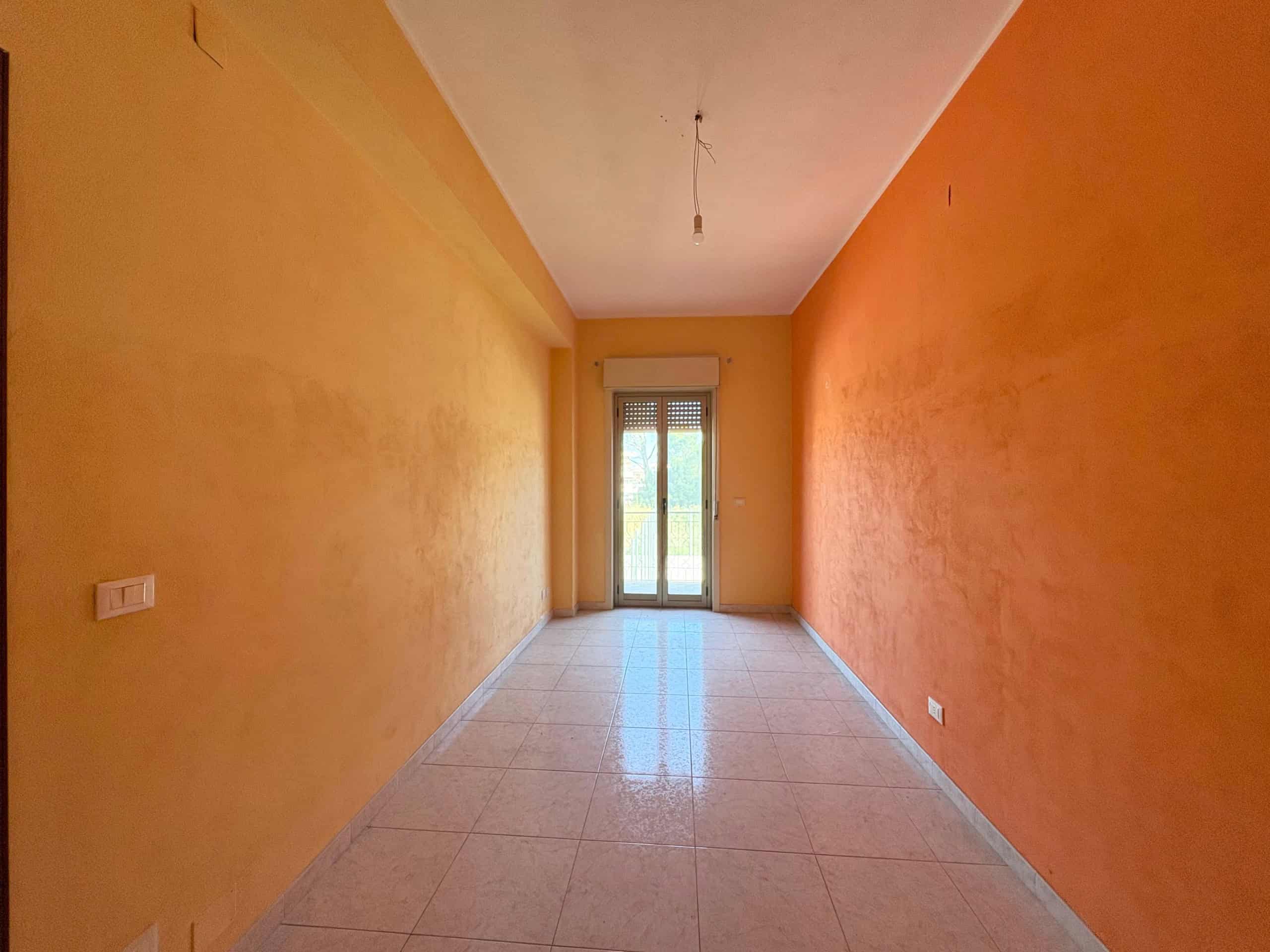 Ampio soggiorno luminoso con pareti arancioni vivaci e porta finestra che apre su un balcone, ideale per la vendita o affitto di immobili residenziali.