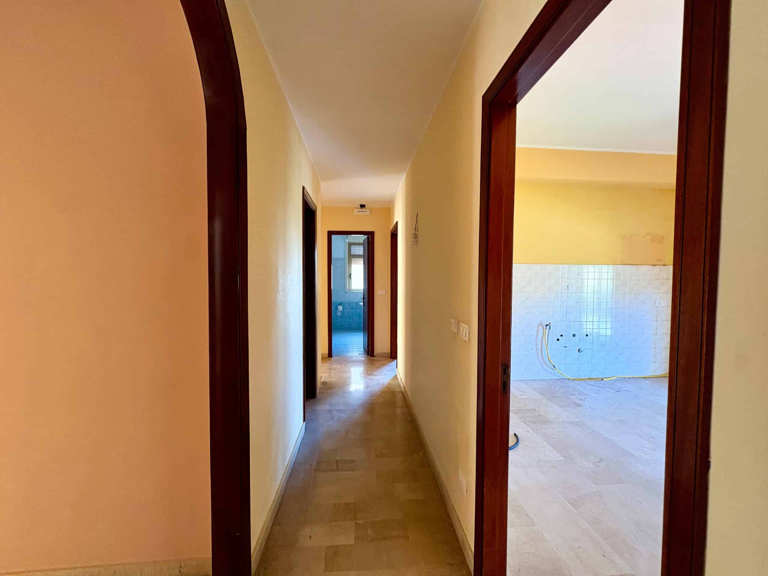 1. Corridoio di un appartamento in fase di ristrutturazione con pareti color pesca e avvolgibili chiusi, vista verso le stanze luminose e il pavimento in parquet.