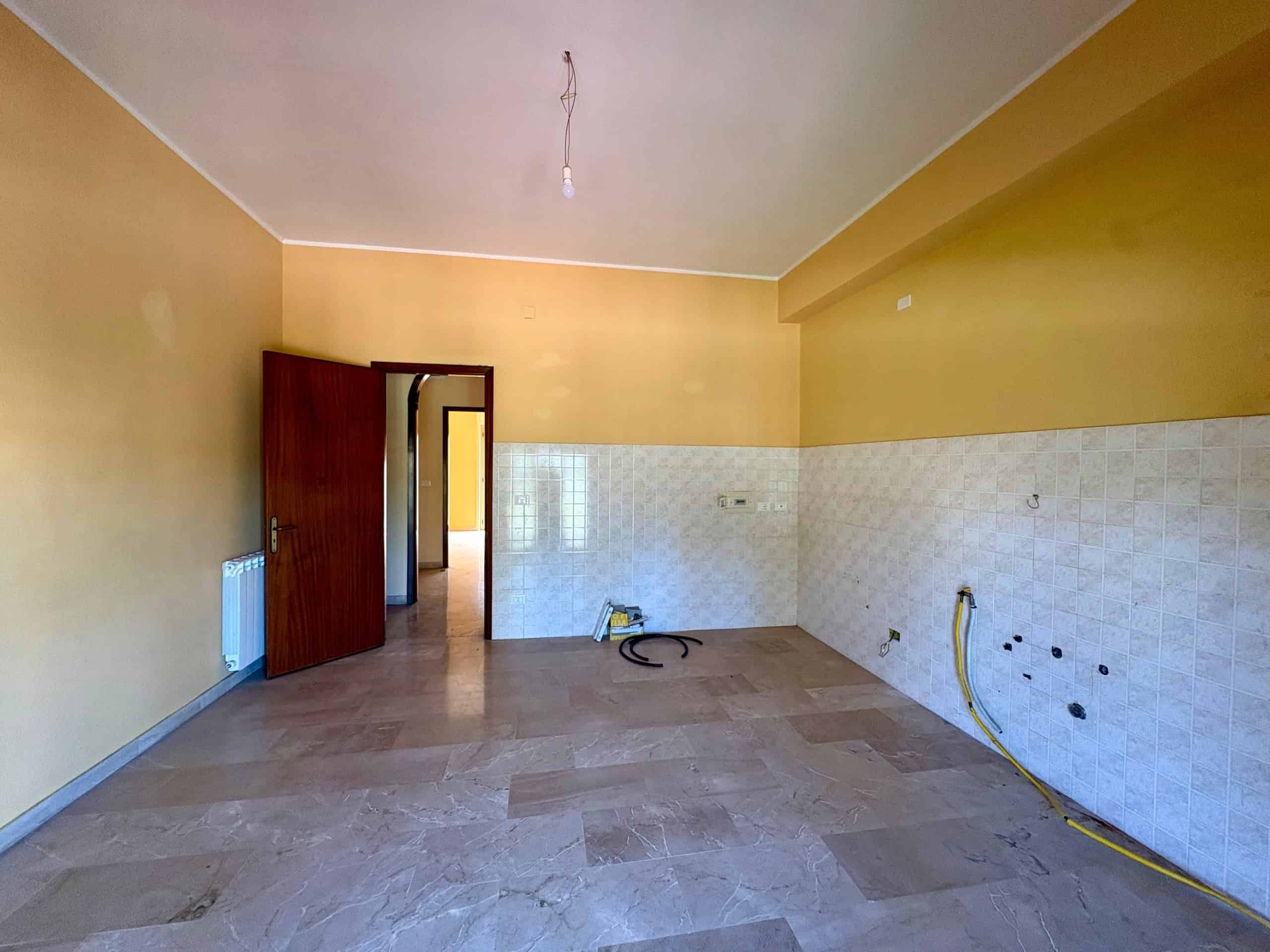 1. Ambiente cucina in fase di ristrutturazione, pareti gialle, pavimento in marmo, con prese e tubi poca luce naturale, pronto per essere arredato e personalizzato.