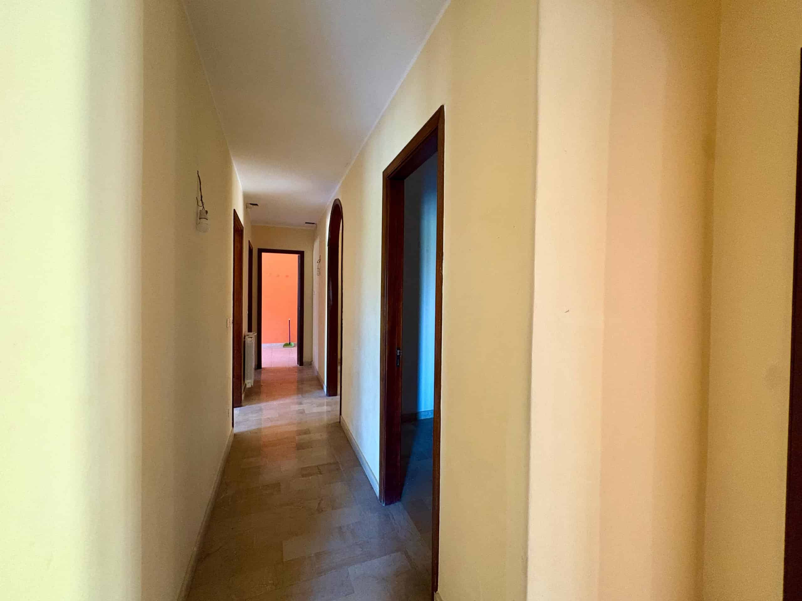 Corridor luminoso di casa in stile classico con pareti color crema e porte in legno, ideale per appartamenti in vendita o affitto. Perfetto esempio di design abitativo funzionale e accogliente.
