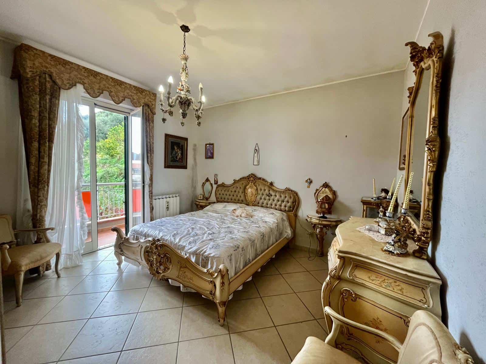 Ampio camera da letto classica con letto in stile vintage, armadi e mobili d'epoca, balcone con vista verde, arredamento elegante e dettagli decorativi ricercati, atmosfere raffinato e tranquillo.