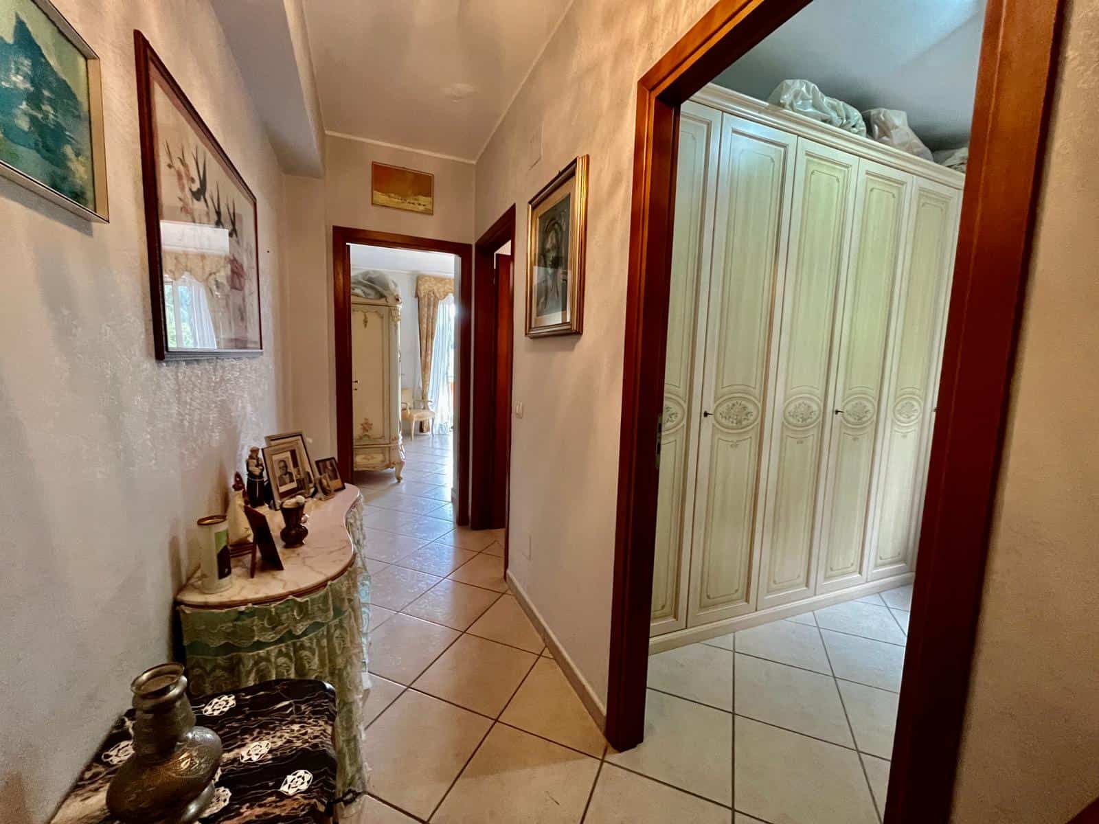 Ampio corridoio in casa con pareti decorate, arredi classici e porte in legno, leading verso camere da letto luminose e arredate in stile elegante, ideale per vivere in comfort e stile.