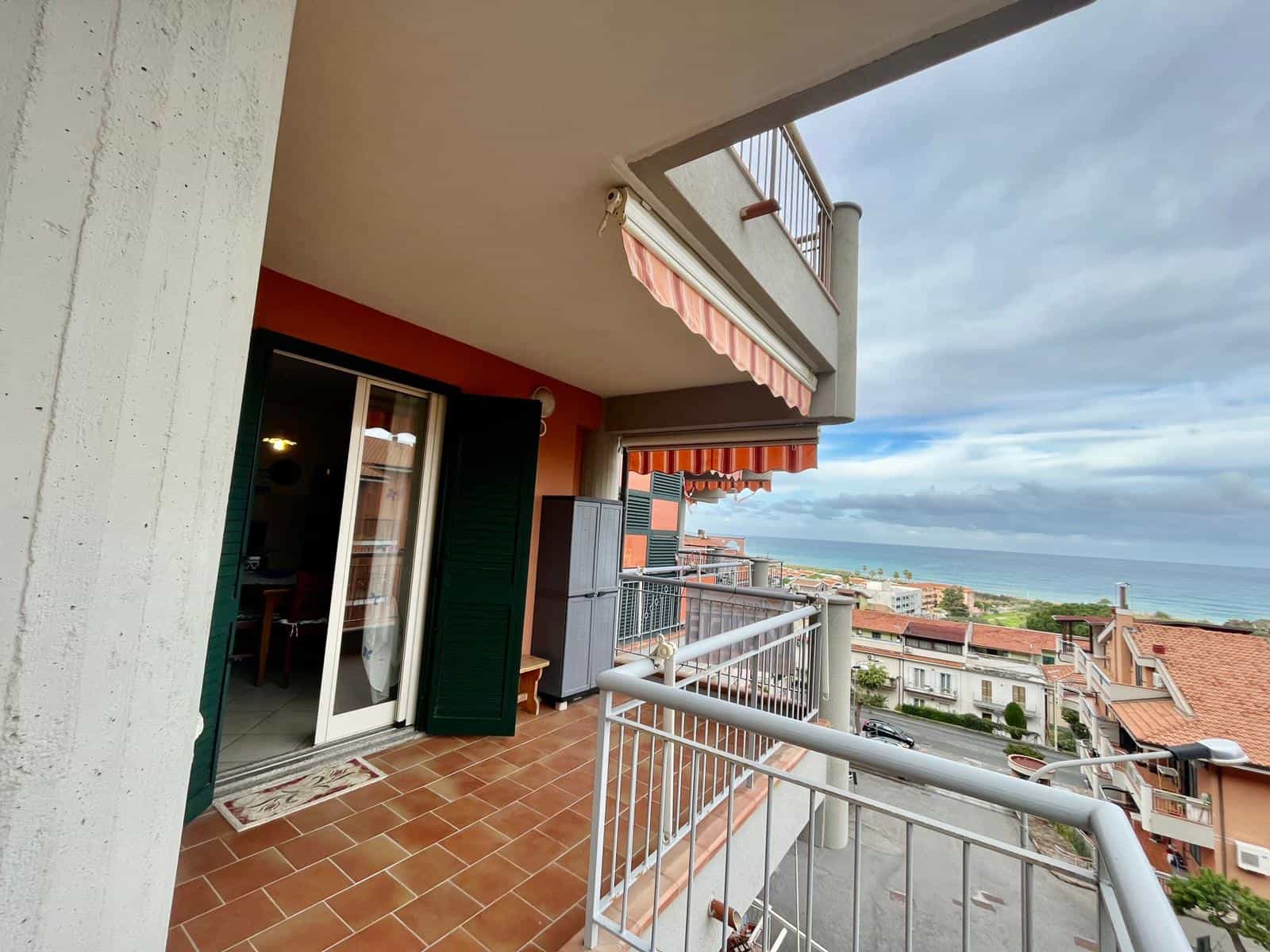 Vista panoramica sul mare dalla terrazza di un appartamento vicino alla spiaggia, con balcone arredato, tende parasole e affaccio su case e strada, ideale per relax e panorama marittimo.
