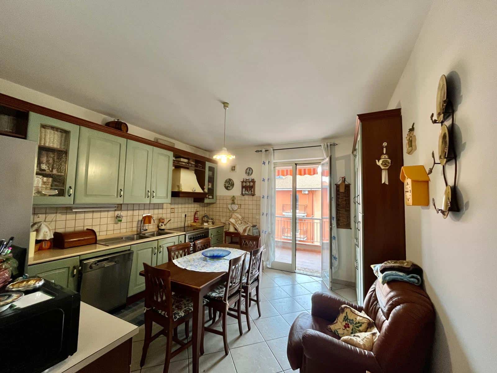 Cucina abitabile con ante verde pastello, possibile accesso al balcone, arredo rustico, ideale per case e appartamenti, con zona pranzo centrale, dettagli vintage e atmosfera accogliente.