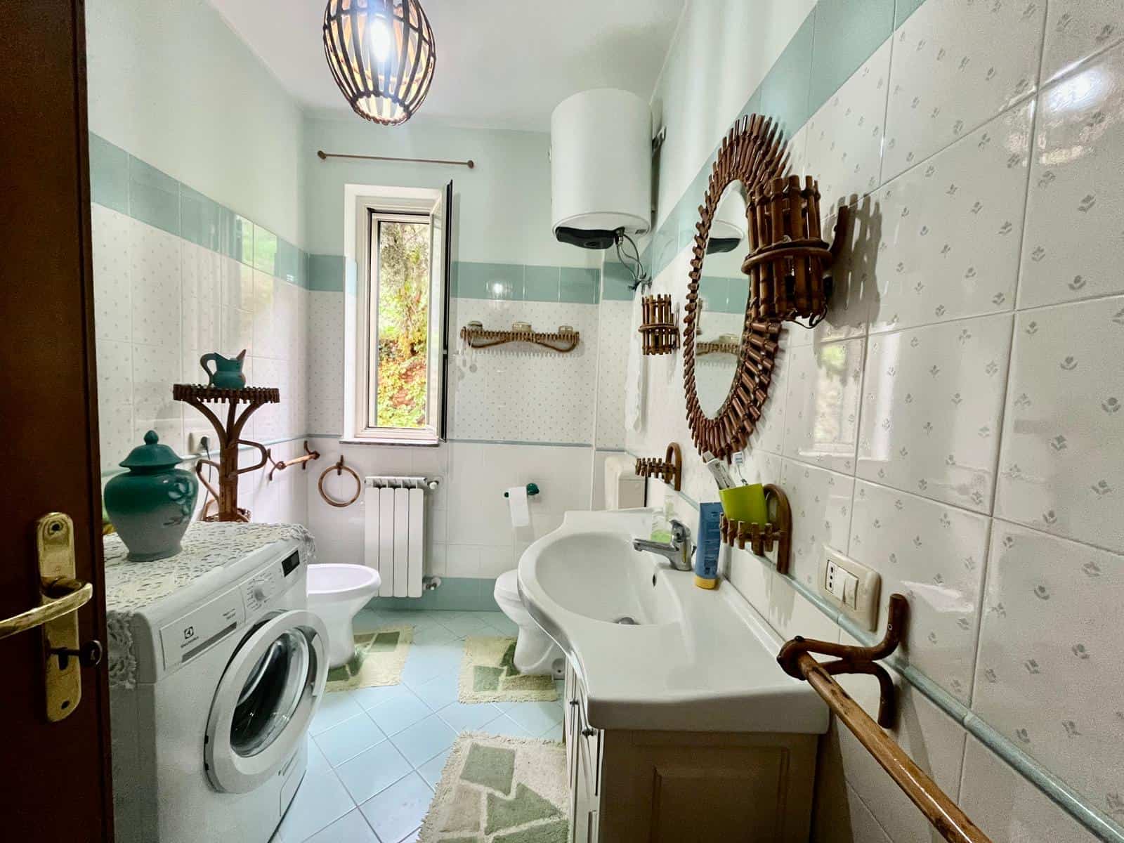 Lavanderia spaziosa con lavatrice, lavabo, finestra e arredi in stile rustico, ideale per la gestione domestica e il massimo comfort. Perfetta per famiglie e abitazioni private.