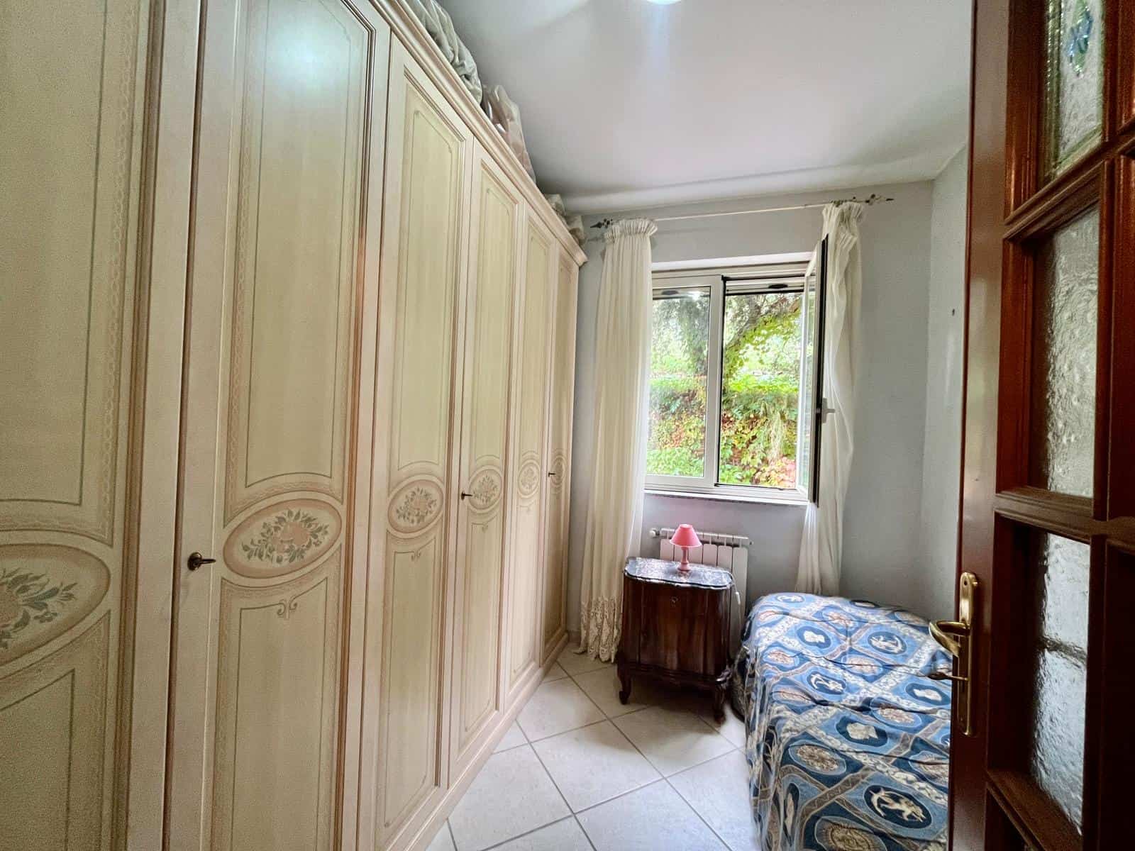Armadio antico con decori floreali, camera da letto luminosa con finestra e vista verde, arredamento classico, stile elegante e accogliente, ideale per case in campagna o appartamenti di charme.