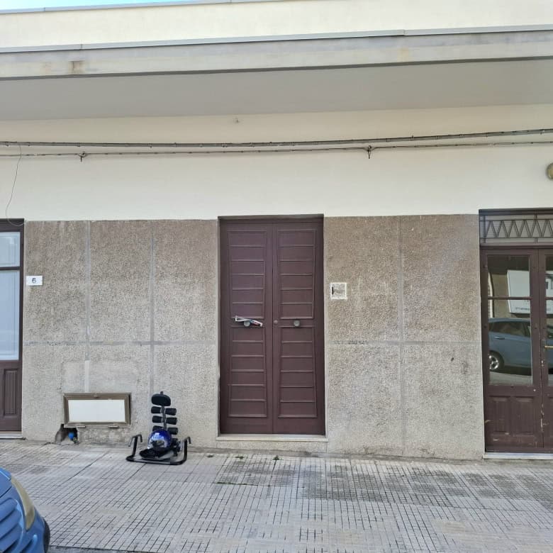 Vetrina e ingresso di un appartamento in vendita, stabile residenziale moderno con porte in legno e pareti in pietra, vicino a parcheggio e strada urbana, perfetto per investimento immobiliare a Napoli.