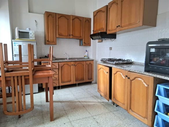 Lavanderia con mobili in legno, cucina compatta con piano in granito, elettrodomestici essenziali, scaffali e utensili da cucina, ambiente funzionale e accogliente.