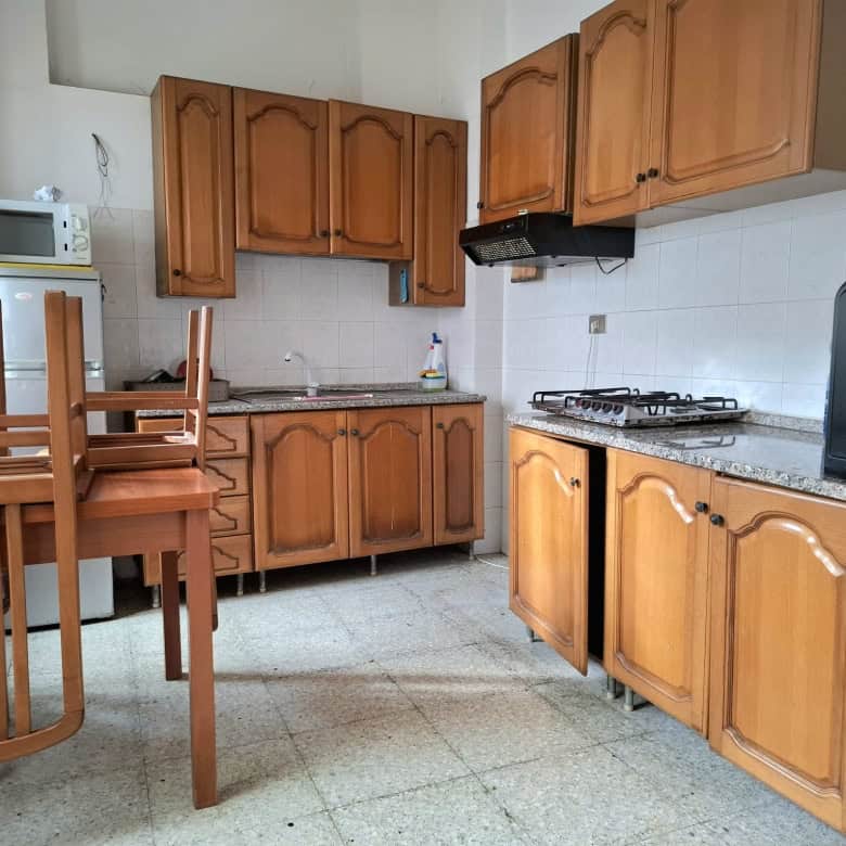 Lavanderia con mobili in legno, cucina compatta con piano in granito, elettrodomestici essenziali, scaffali e utensili da cucina, ambiente funzionale e accogliente.