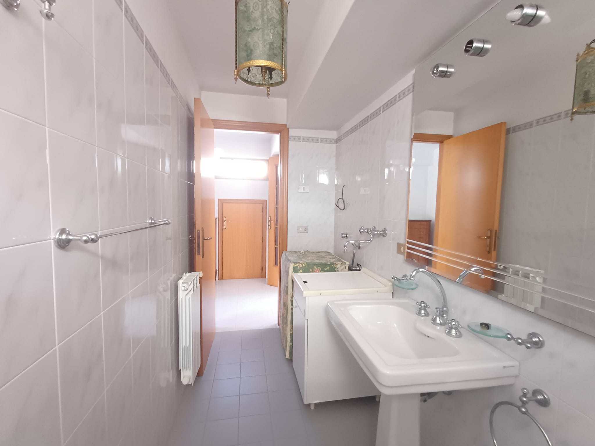 Lavabo da bagno con specchio grande, piastrelle bianche, dettagli in metallo, dettagli vintage, atmosfera luminosa, NextCasa immobile, arredo bagno classico, bagno funzionale, stile semplice e pratico, ambiente abitabile, casa in vendita o affitto.