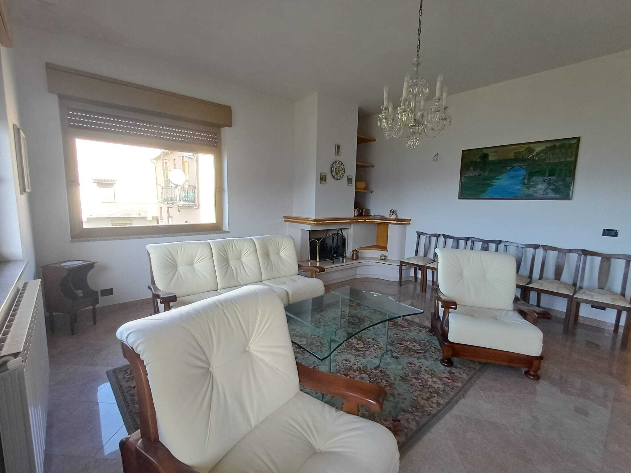 Soggiorno elegante con sedie e divani in pelle color avorio, camino aurnico, e lampadario in cristallo, ambiente luminoso con ampio finestra e vista sulla città, arredamento tradizionale e dettagli curati.