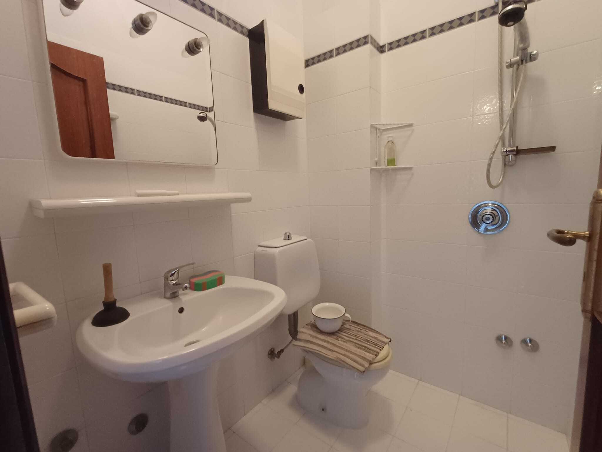 Lavabo e bagno con doccia in stile semplice, con accessori essenziali e pareti rivestite in ceramica bianca, ideale per appartamenti in vendita o affitto.