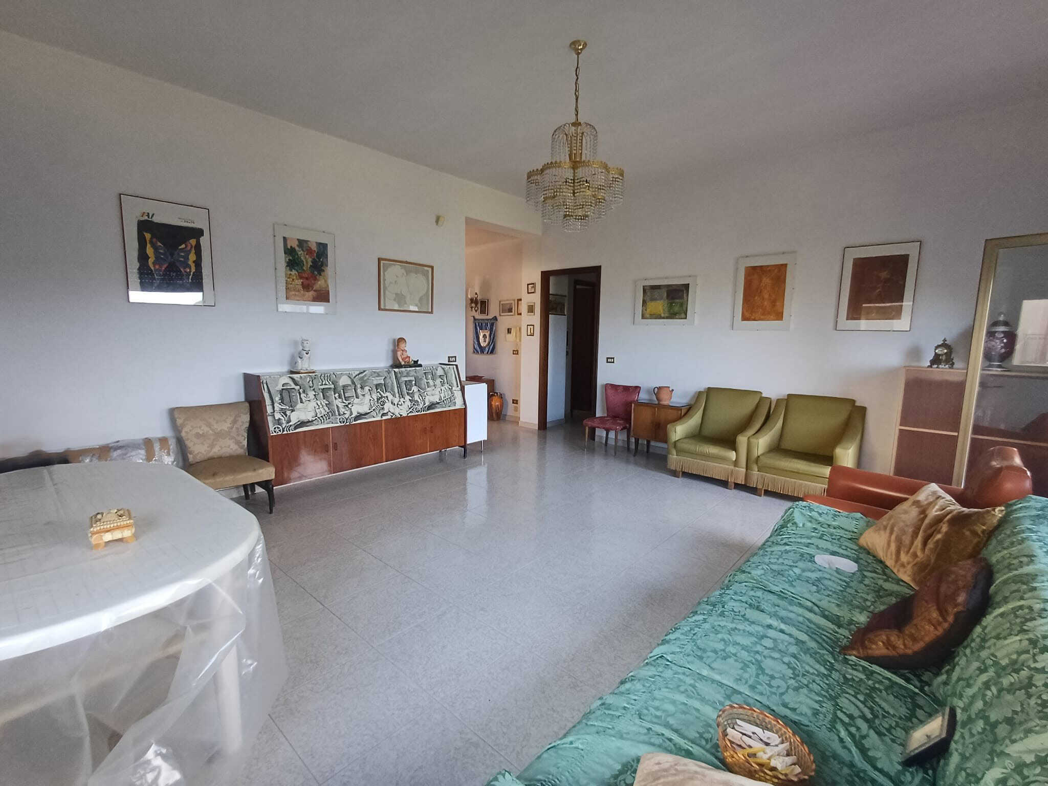 Ampio soggiorno con mobili vintage, pareti decorate con opere d'arte, divani e poltrone colorate, lampadario in cristallo, atmosfera accogliente e elegante, ideale per vivere momenti di relax e convivialità.