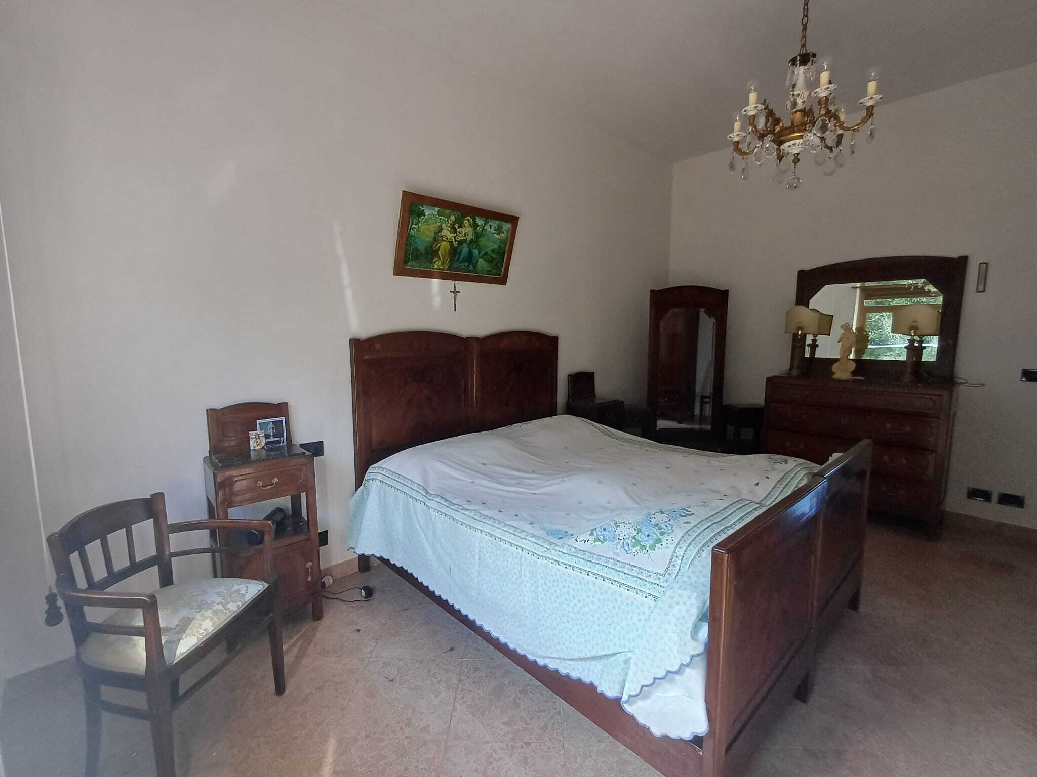 Ampa;; Camera da letto classica con letto in legno, specchio e mobili vintage, illuminata da lampade e con lampadario in cristallo, arredo elegante e caldo, ideale per case di charme e residenze storiche.