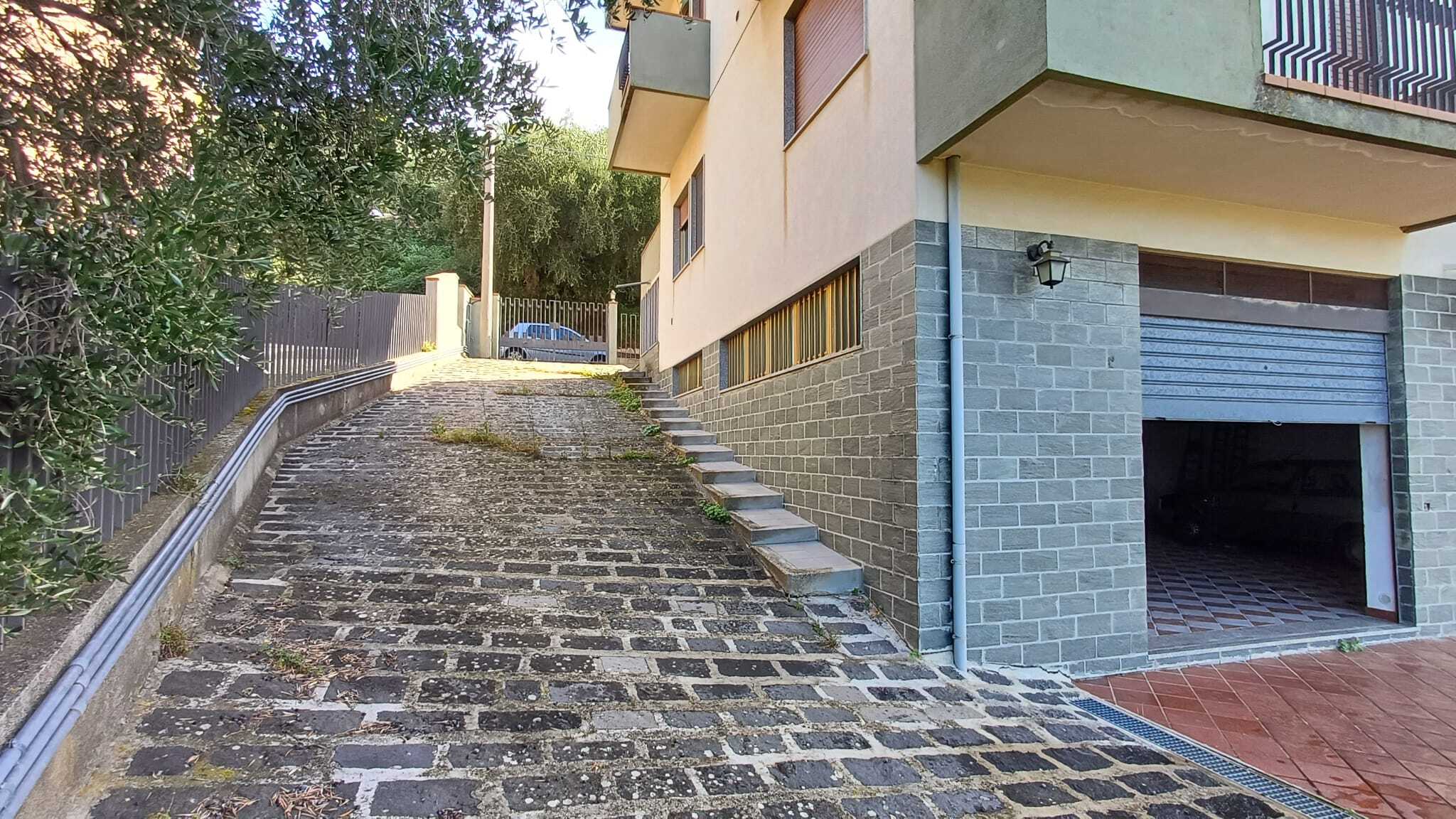 Spsecchio di strada in pietra con accesso alla garage, vista esterna di un edificio residenziale contemporaneo.