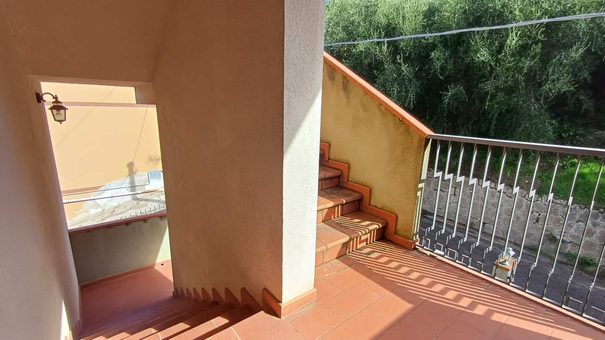 Scala esterna in mattoncini e terrazza con ringhiera in metallo, vista su zona verde e muro di pietra, ambiente di casa in stile mediterraneo, ideale per relax e vita all'aperto.