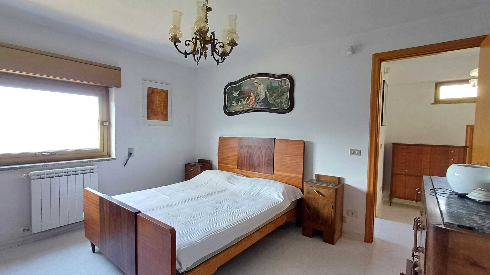Letto matrimoniale in camera da letto con mobili in legno e decorazioni classiche, grande finestra con vista luminosa, stile elegante e tradizionale, ideale per appartamenti o case in vendita e affitto.