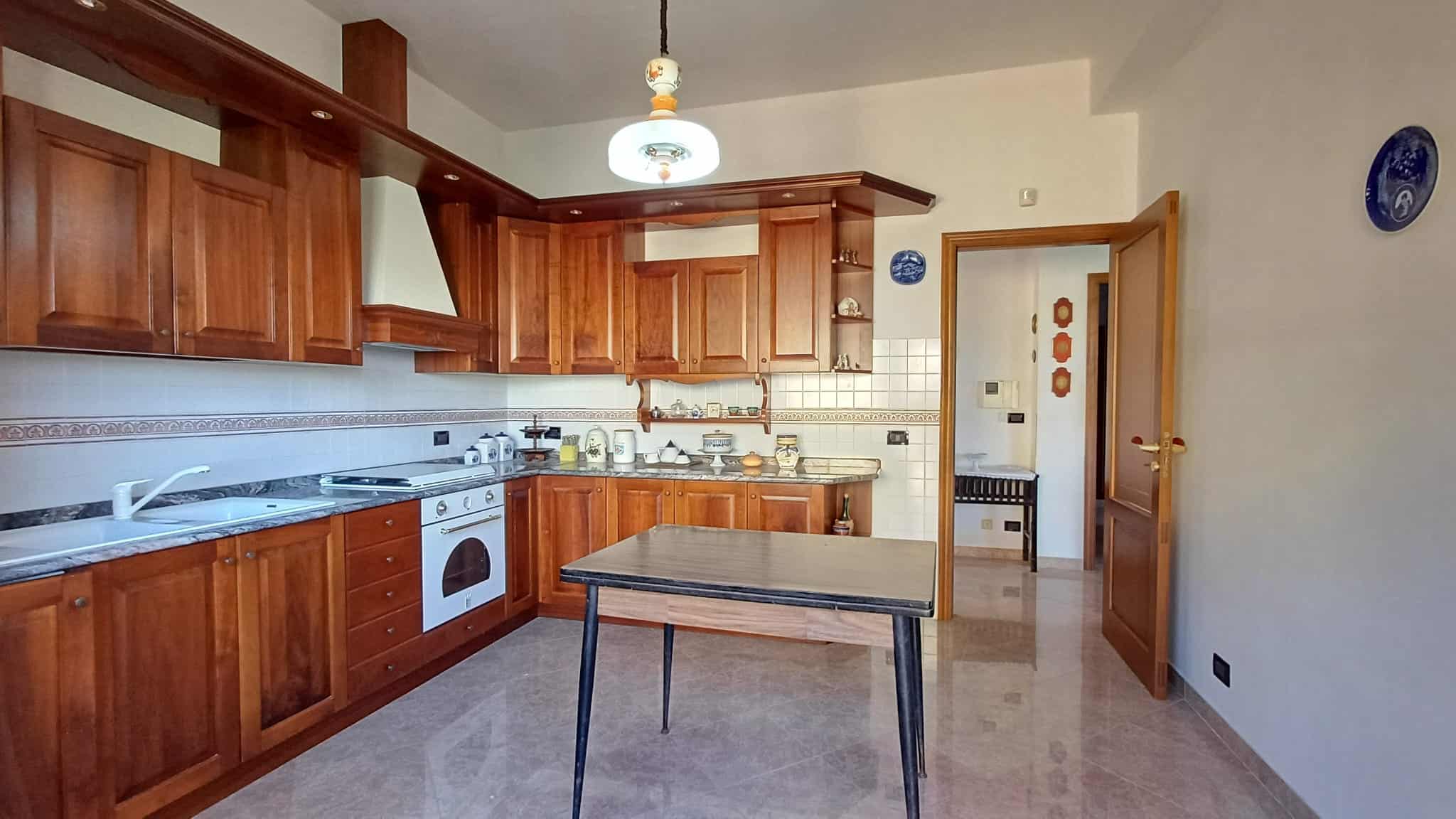 Lavanderia in cucina con ante in legno, piano in marmo, forno e stoviglie, decorazioni in stile tradizionale, illuminazione moderna e pareti bianche, ambiente accogliente e funzionale.
