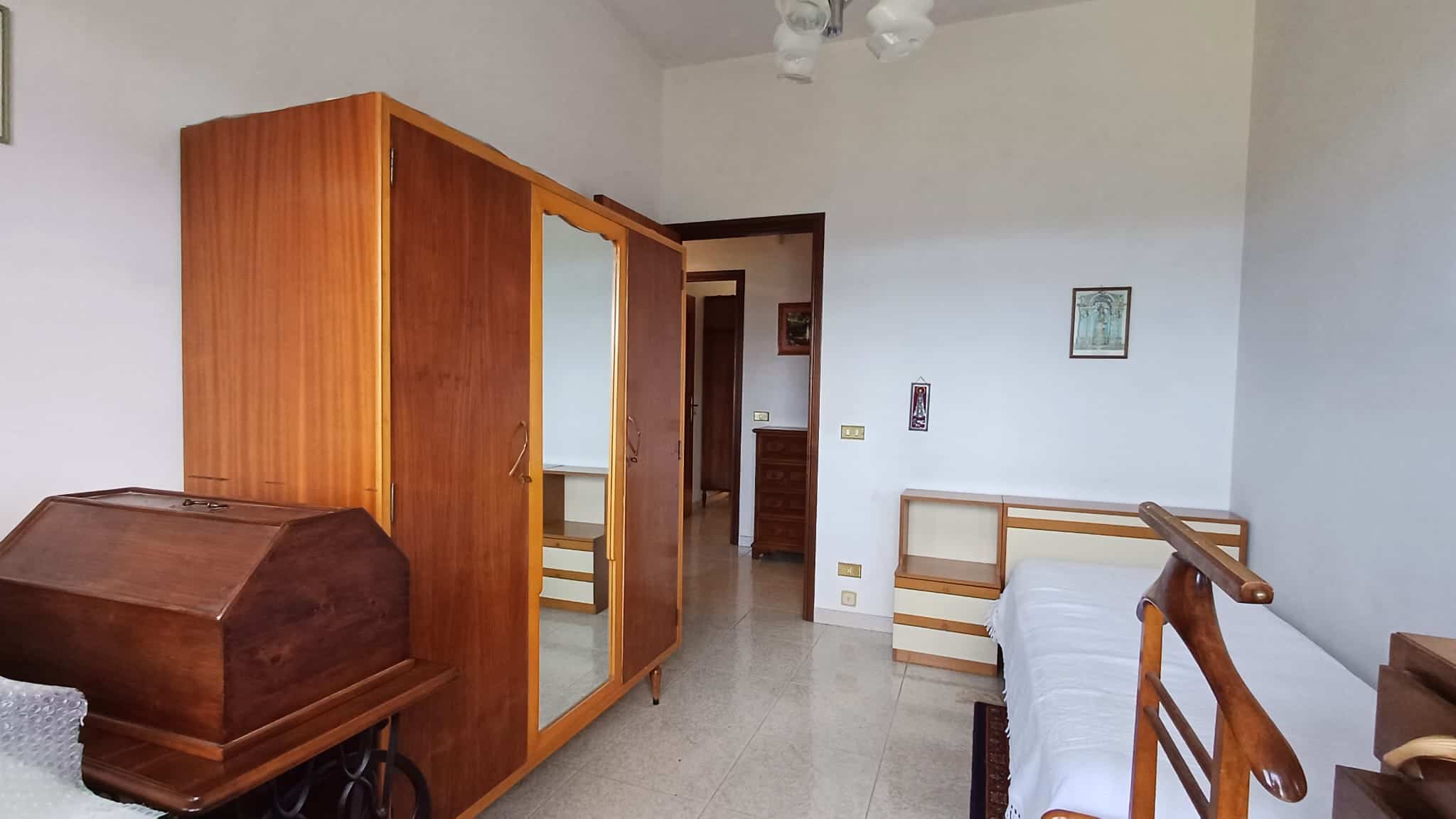 Armadio in stile classico con specchio, camera da letto con letto e comodini in legno, decorazioni semplici e ambientazione accogliente, ideale per una casa in stile tradizionale.