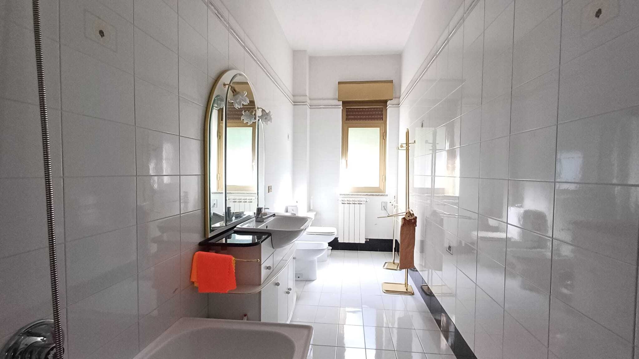 Bagno moderno con sanitari bianchi, lavabo con specchio e finestra, arredi funzionali e dettagli di design, perfetto per abitazioni di qualità.