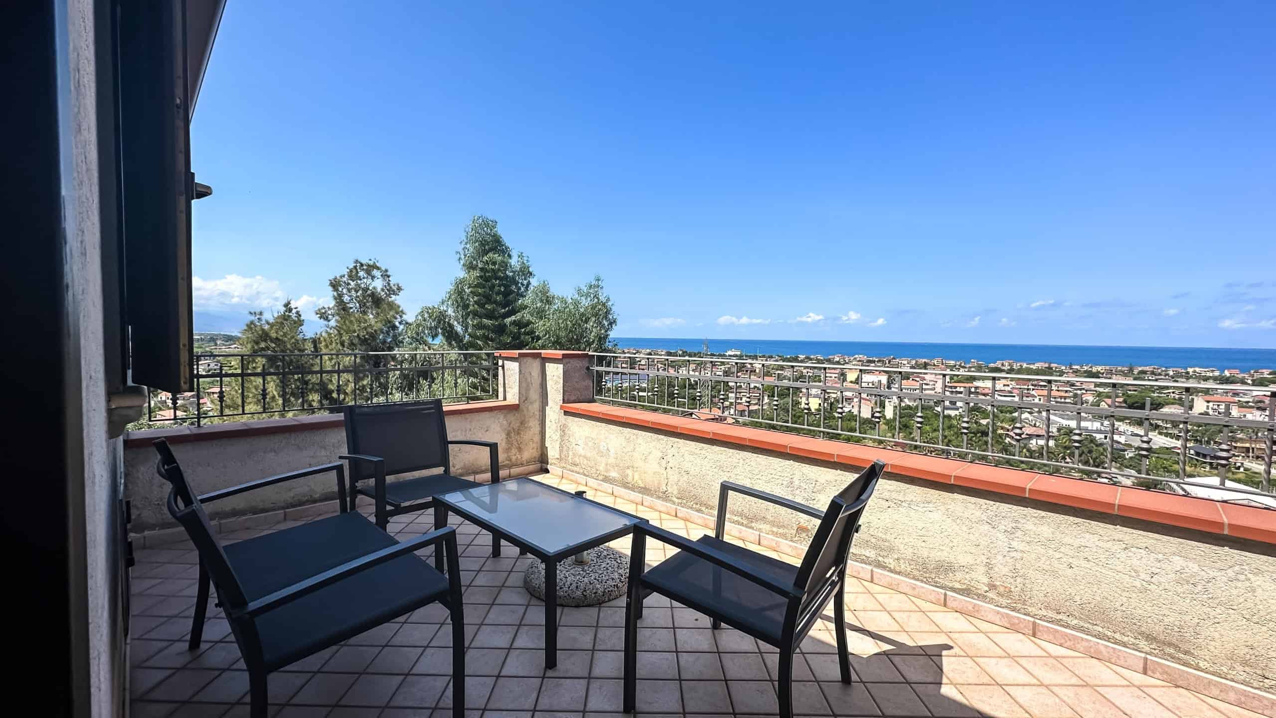 Panoramica della terrazza con mobili da esterno e vista mare, ideale per relax e socializzare in un appartamento NextCasa, in posizione privilegiata vicino alla costa.