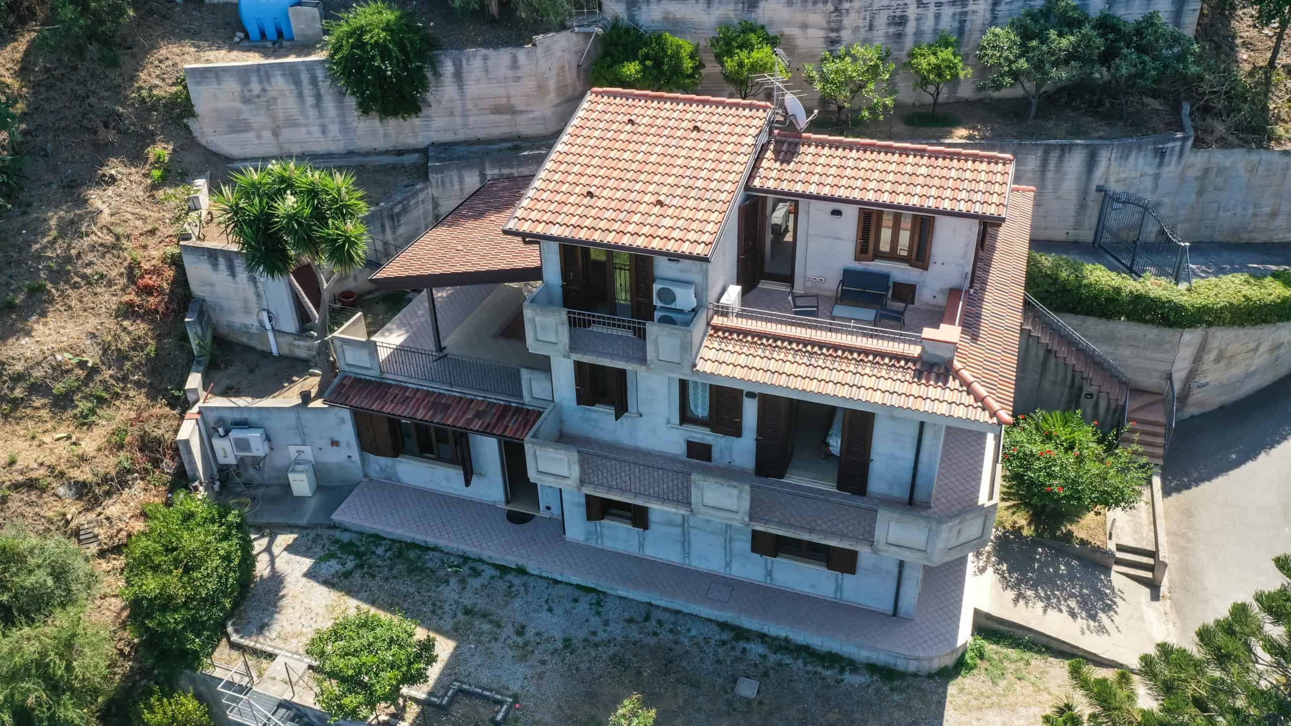 Casa moderna in stile mediterraneo con terrazzi, tetto con tegole e giardino privato, immersa nel verde, ideale per residenza di qualità e benessere.