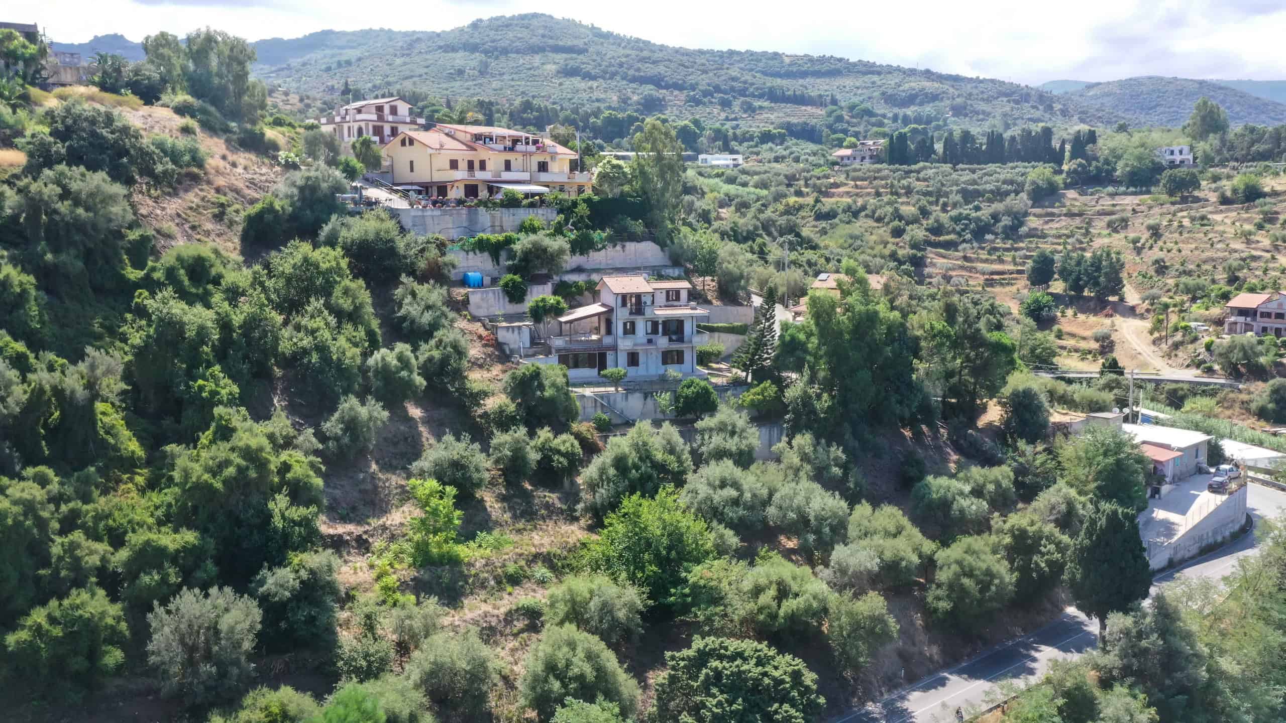 Villetta moderna su collina circondata da natura e verde, con vista panoramica, giardino Lussureggiante, e strada di accesso. Lunghezza dell'immagine: 1740 pixels.