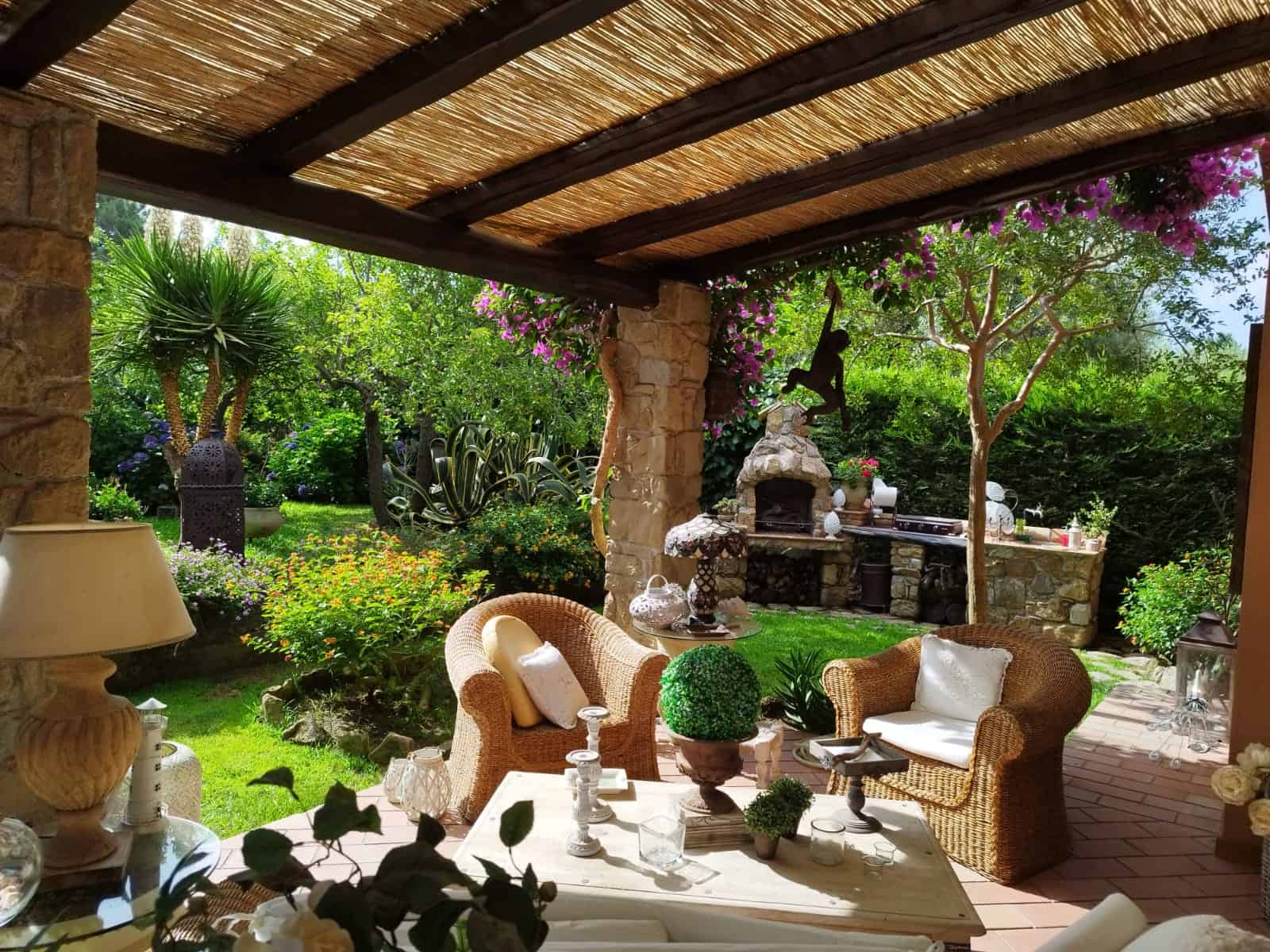 Relaxing outdoor patio with wicker chairs, lush greenery, and vibrant flowers under a woven pergola, ideal for outdoor dining and enjoying nature.