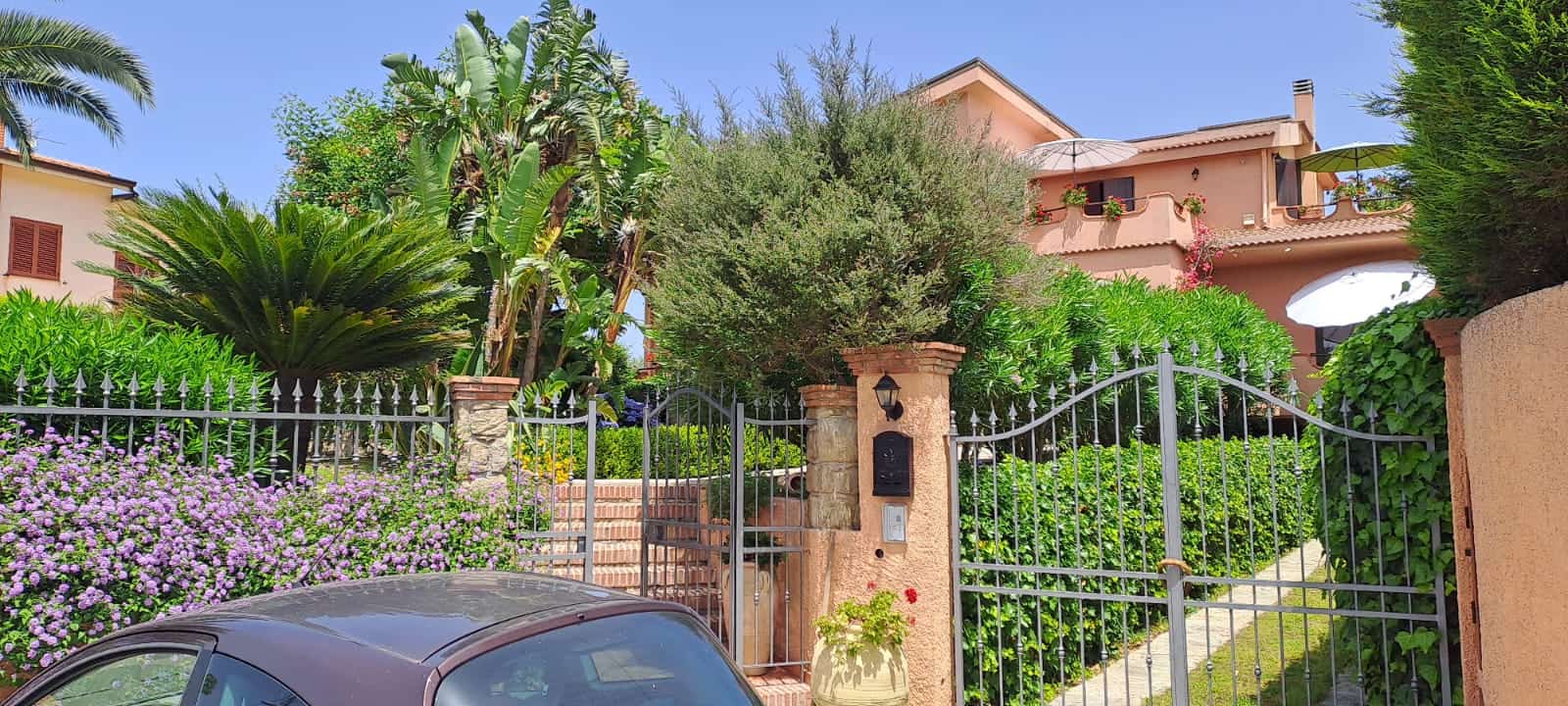 Giardino curato con piante tropicali e fiori colorati davanti a casa nel quartiere residenziale di lusso NextCasa, atmosfera mediterranea e vista panoramica.
