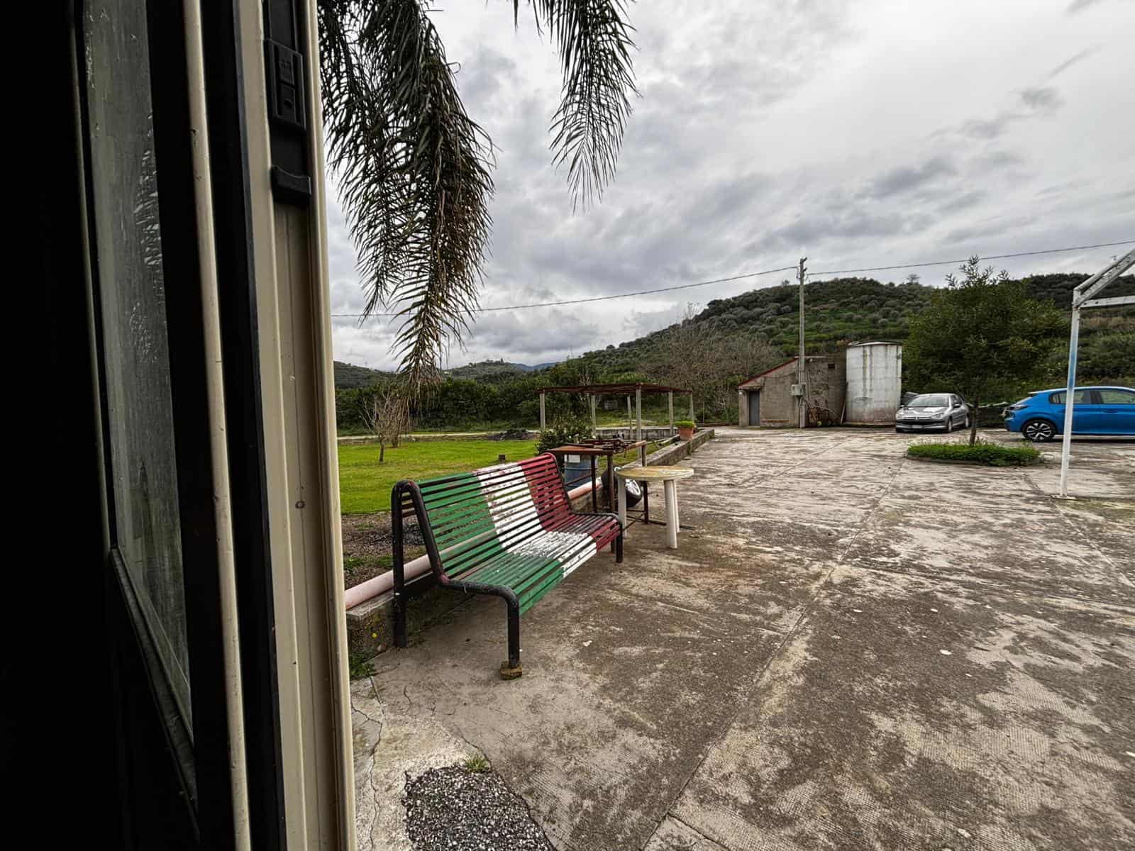Veranda rustica con panchina decorata con i colori della bandiera italiana, vista su campagna e montagne, in un ambiente naturale e tranquillo, ideale per relax e momenti all'aperto.