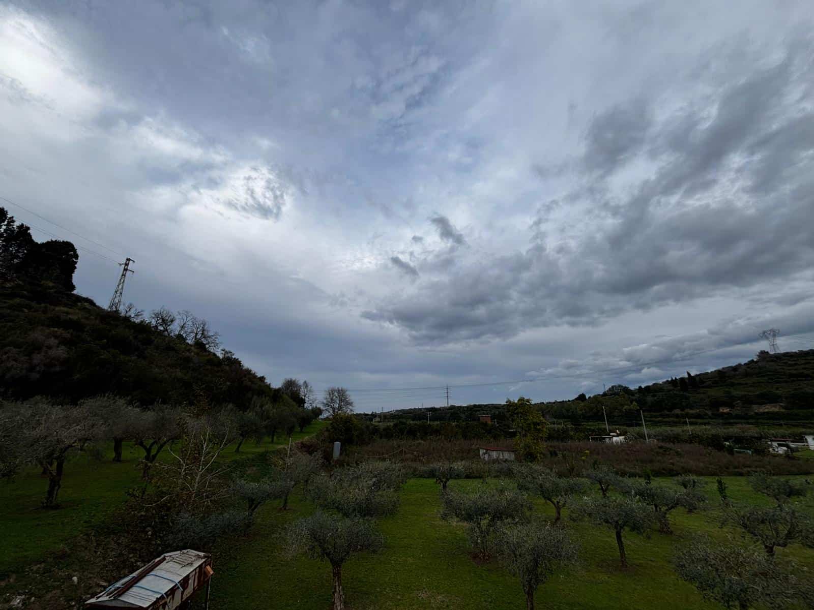 Vasta vista di un paesaggio rurale con alberi e colline sotto un cielo nuvoloso, ideale per investimenti immobiliari e terreni rustici.