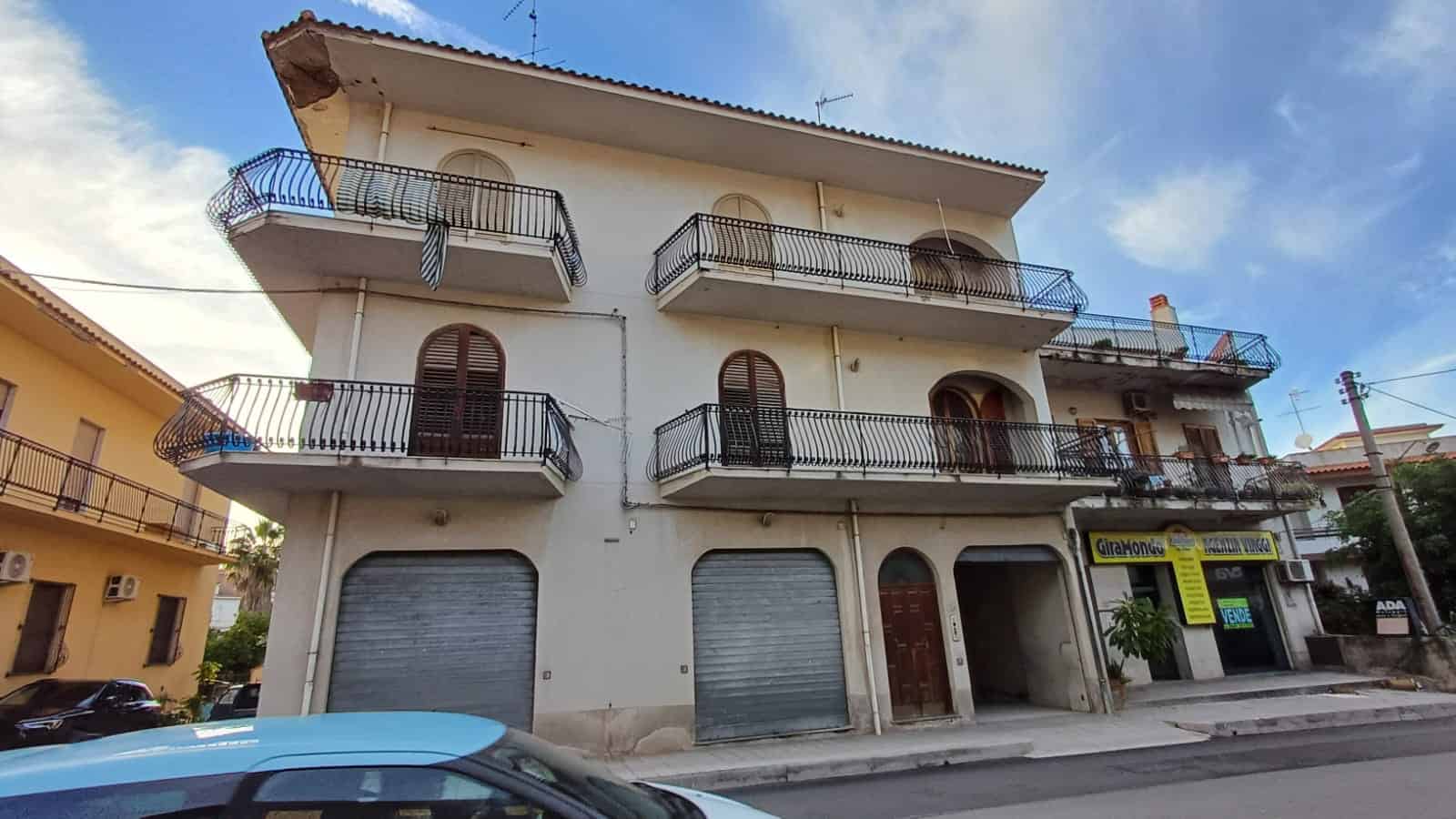 Balconi panoramici e facciata di edificio residenziale con negozio al piano terra, ambienti ben disposti e stile classico, situato in zona urbana con traffico veicolare.