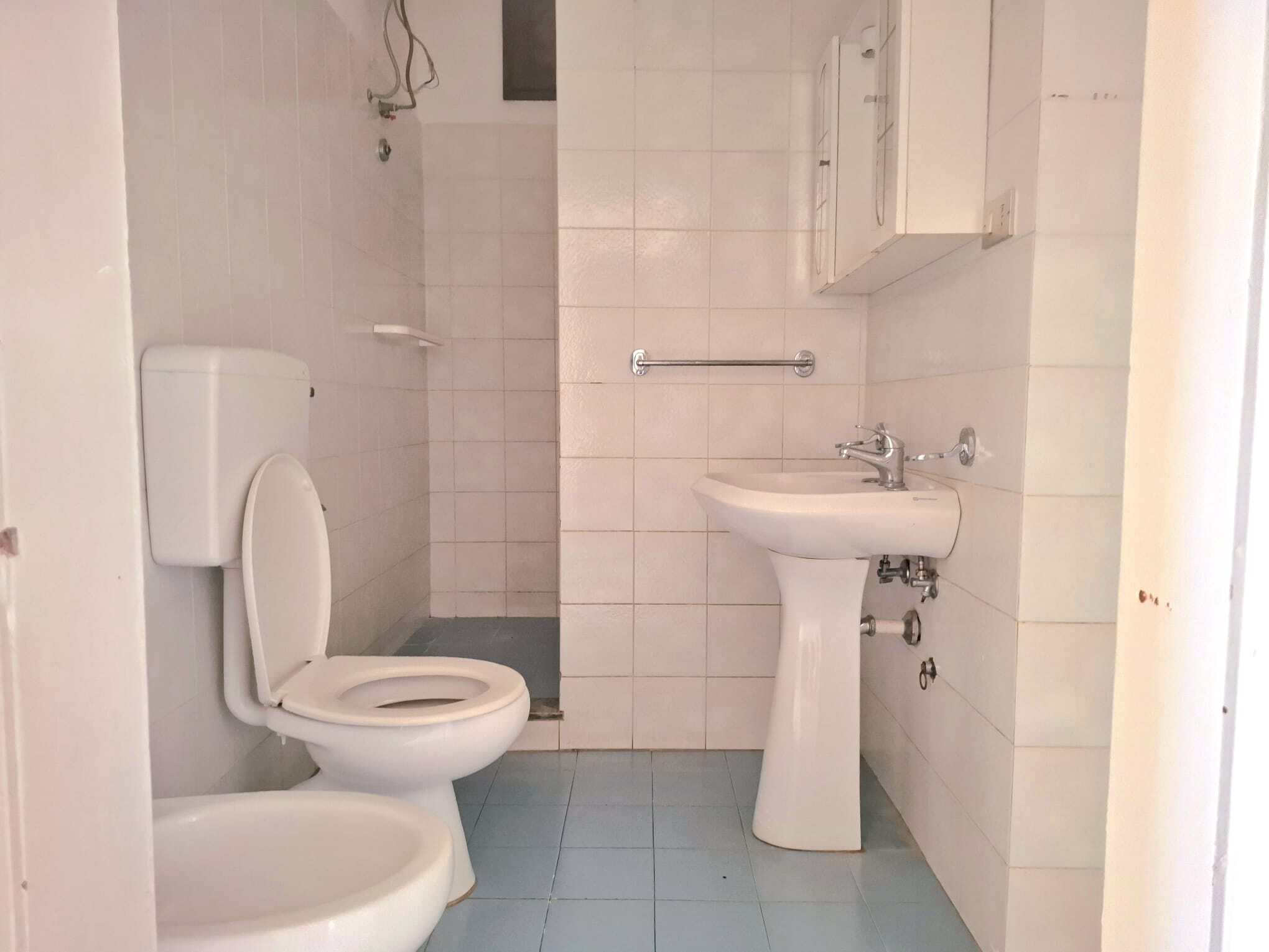 Bagno semplice con WC, lavabo e armadietto, pareti e pavimenti in piastrelle chiare, ambiente funzionale e pulito, ideale per abitazioni moderne e pratiche.