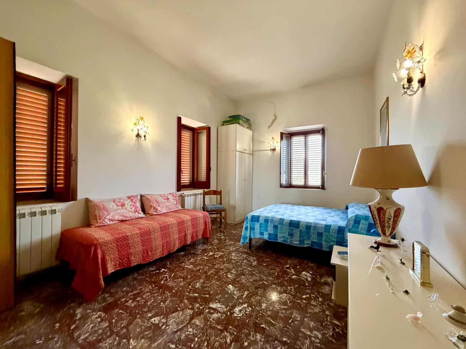 Ampia camera da letto con due finestre, letto matrimoniale e divano, arredamento semplice e luminoso, ideale per soggiorni confortevoli e rilassanti.