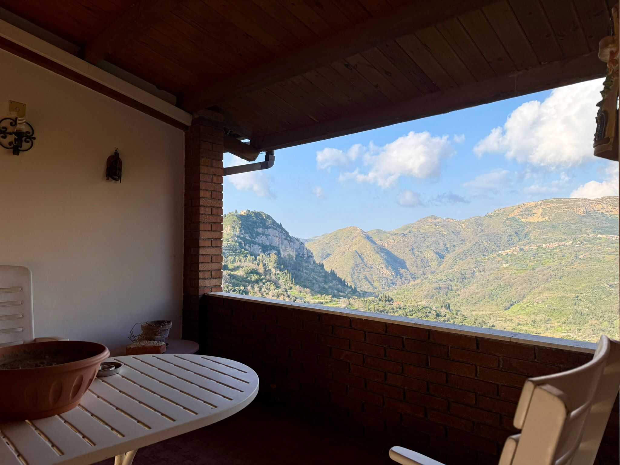 Balcone con vista panoramica sulle montagne e paesaggi naturali, arredato con tavolo in plastica e piante decorative, ideale per relax e momenti di convivialità all'aperto.