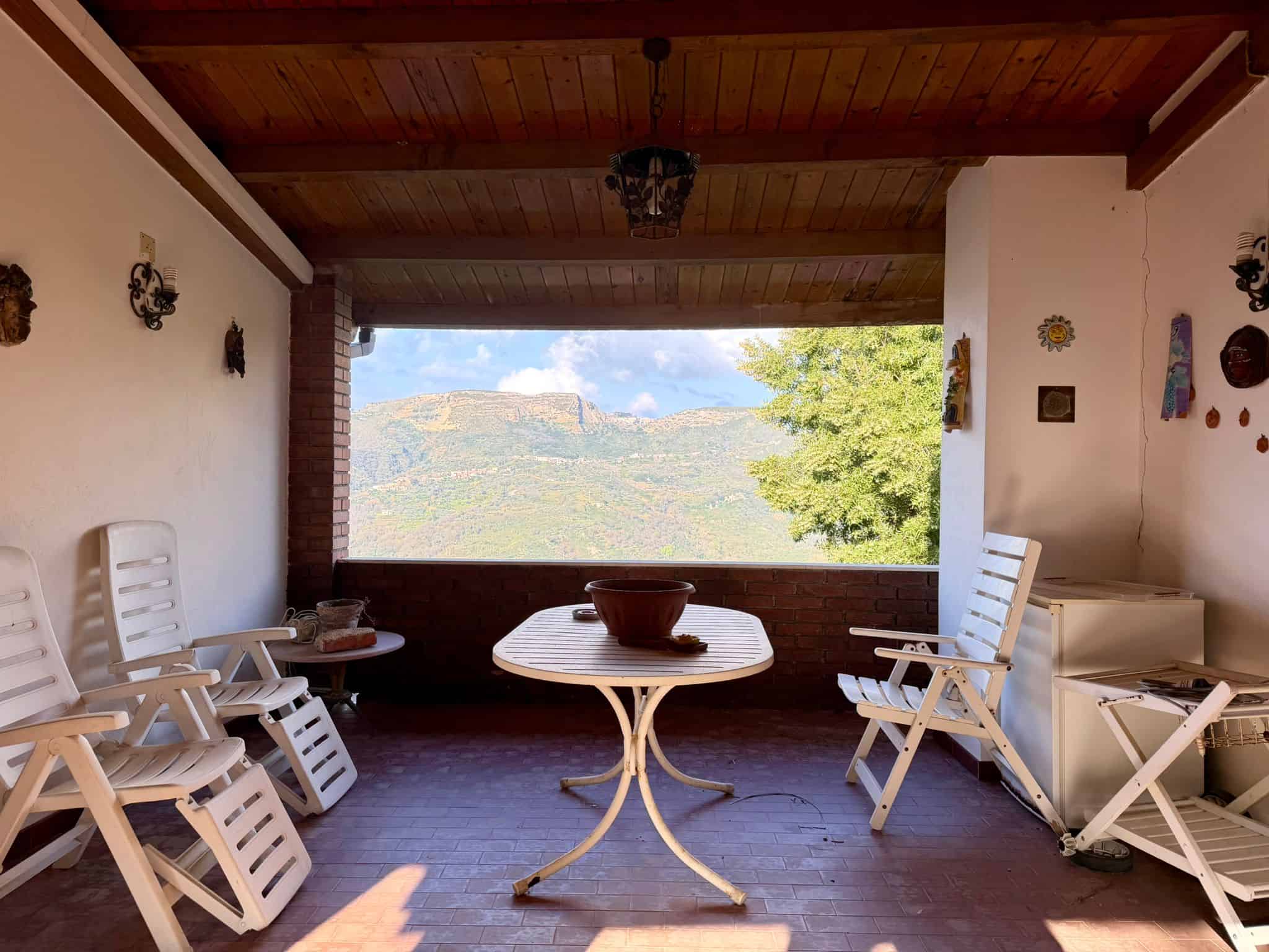 Godere di una vista panoramica sulla natura dalla veranda di una casa in stile rustico, con mobili in legno e decorazioni tradizionali, ideale per relax e momenti di convivialità all'aperto.