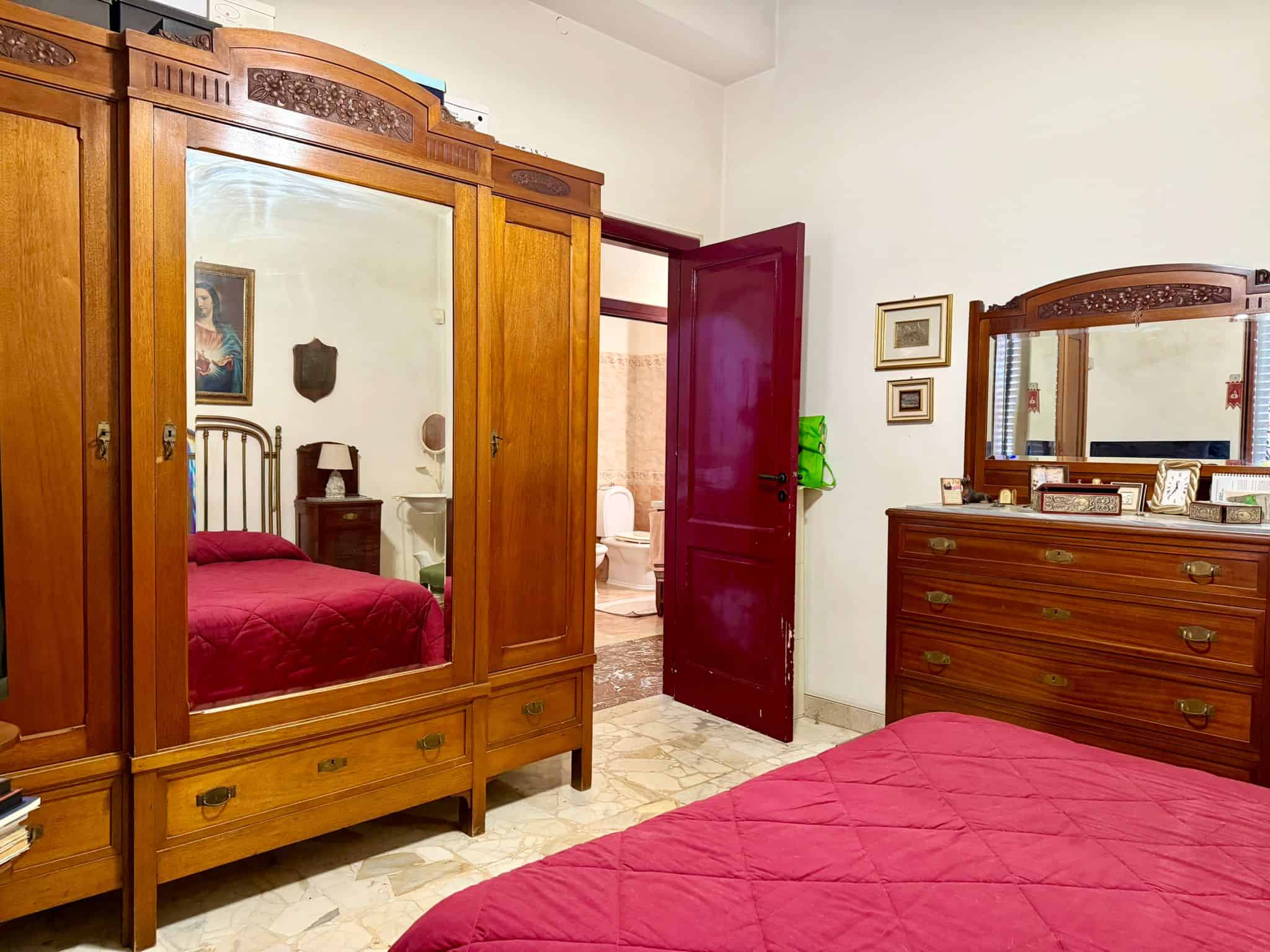 Armadio in legno con specchio e camera da letto con letto matrimoniale e comò in stile classico, vista da una stanza in stile vintage.