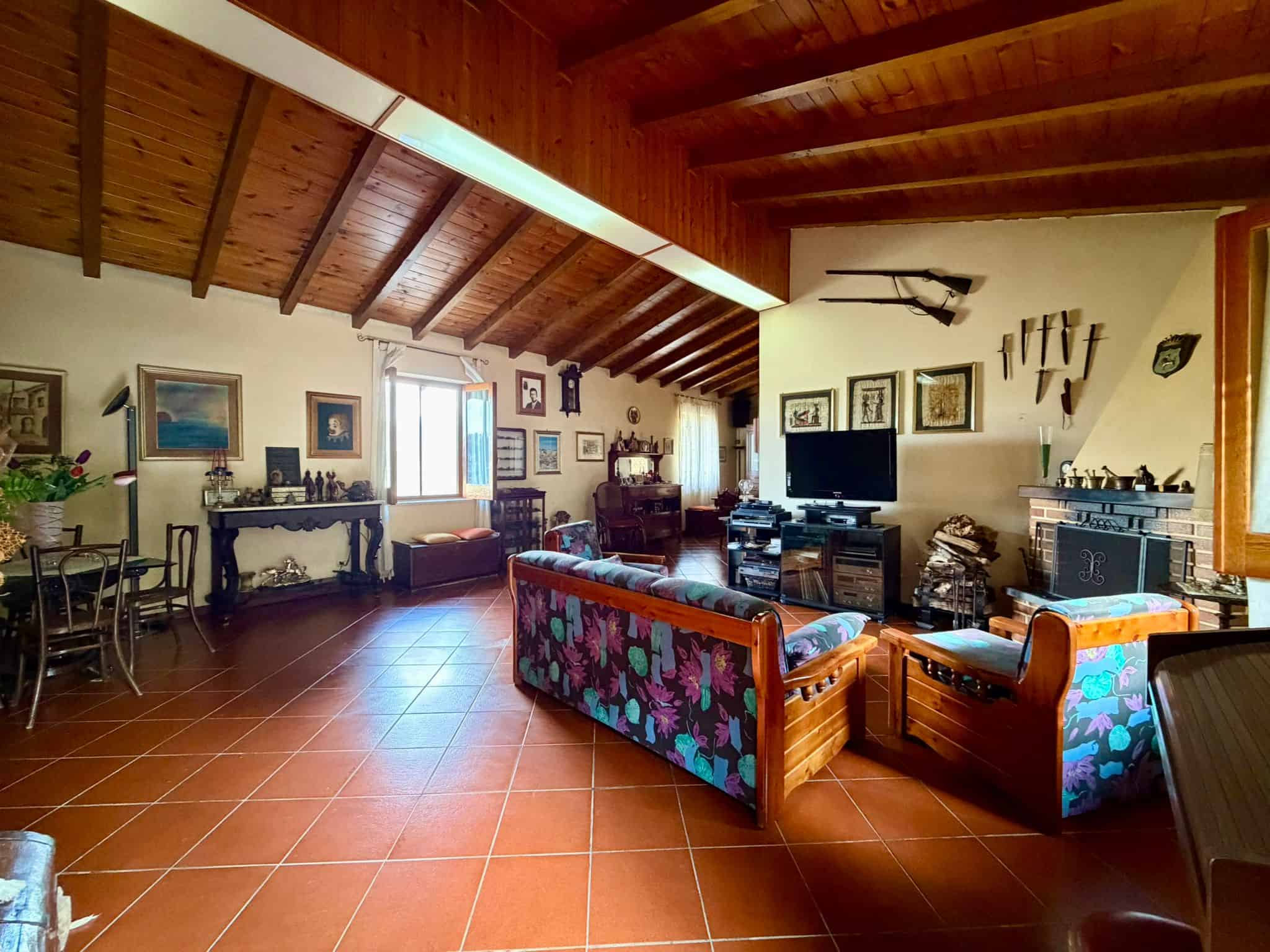 Ampia zona living con soffitto in legno, arredi vintage e pareti decorate con quadri e oggetti d'arte, ideale per vivere momenti di relax e convivialità in un ambiente accogliente e caratteristico.
