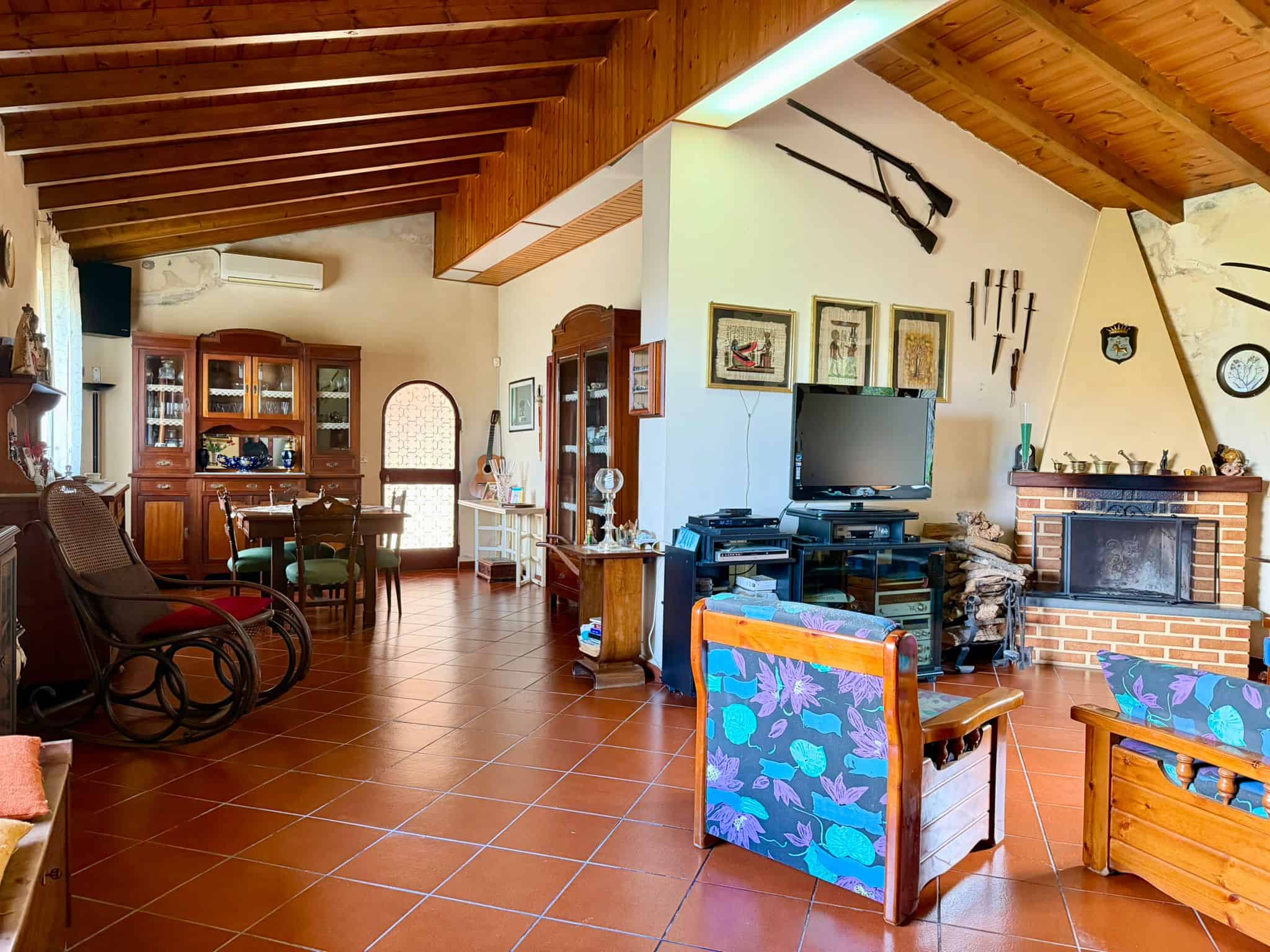Interno soggiorno con soffitto in legno, camino in mattoni, mobili in stile classico e decorazioni vintage, ambiente accogliente e spazioso.