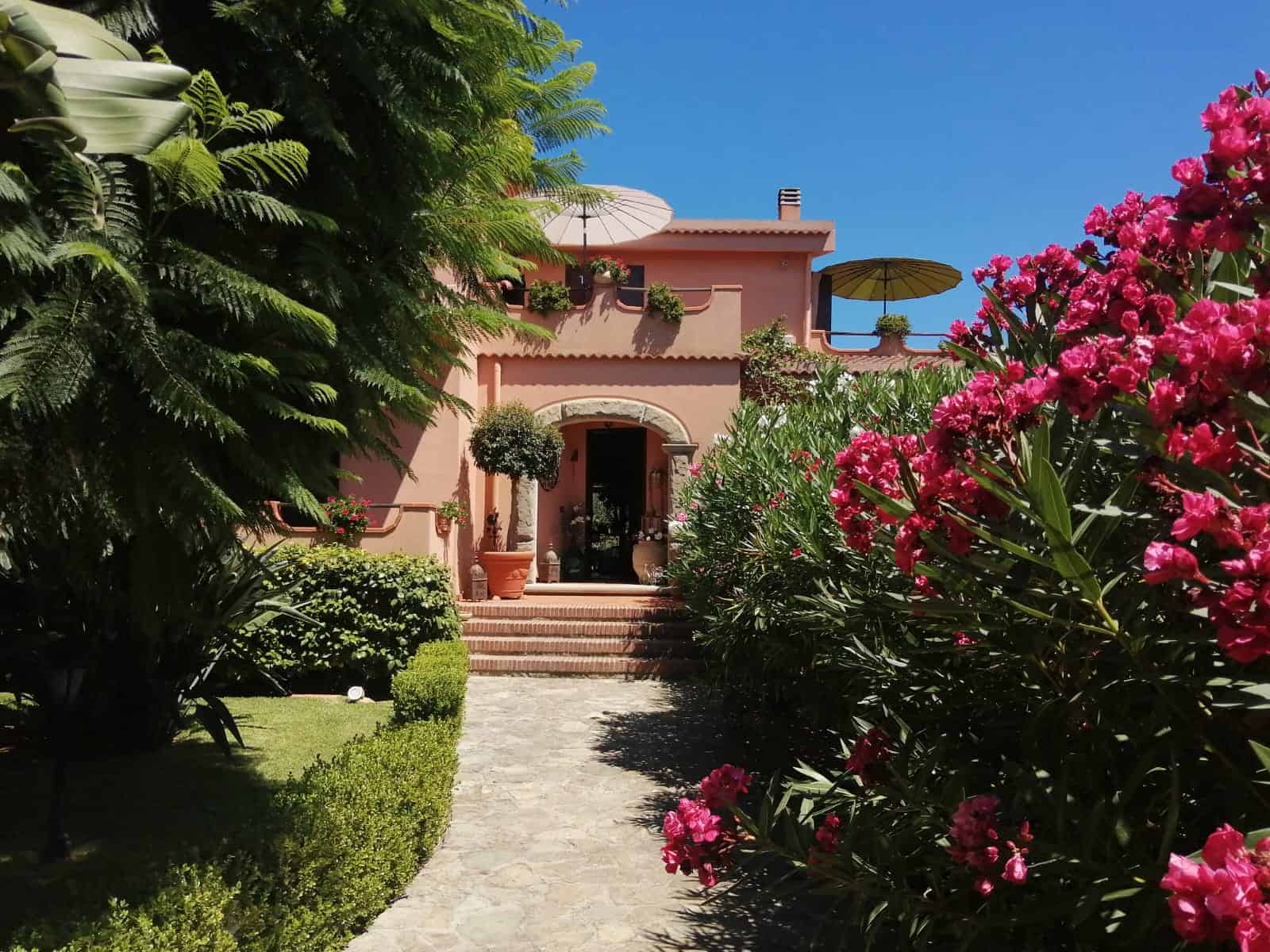 Villa di lusso con giardino curato e terrazza panoramica in Toscana, ideale per relax e eventi esclusivi. Elegante stile mediterraneo con piante ornamentali e ombrelloni. Perfetta soluzione immobiliare NextCasa.