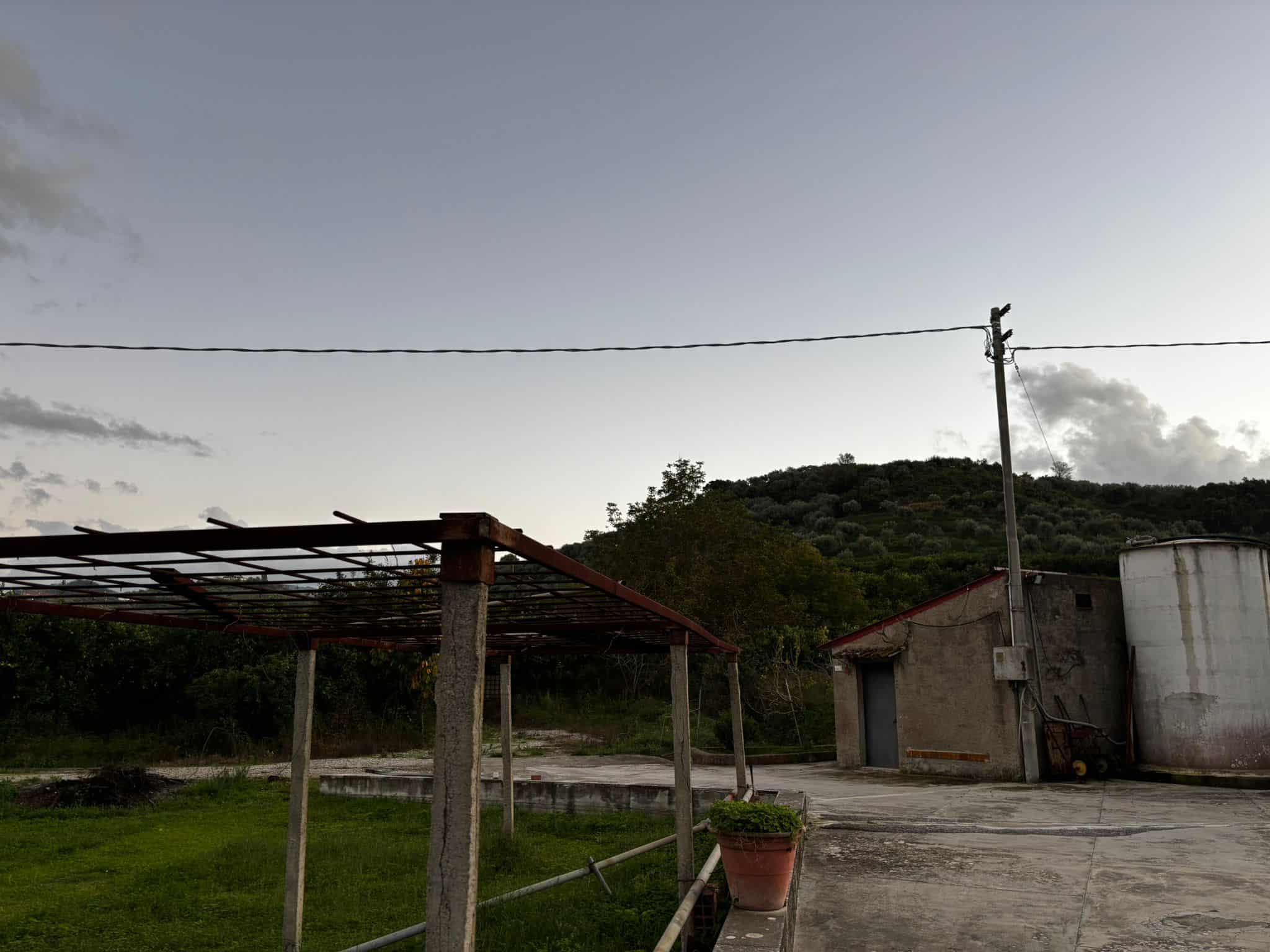 Vecchio contesto rurale con struttura in cemento e legno, ambiente esterno con vegetazione e colline sullo sfondo, perfetto per immagini legate a immobili rustici e agriturismi NextCasa.