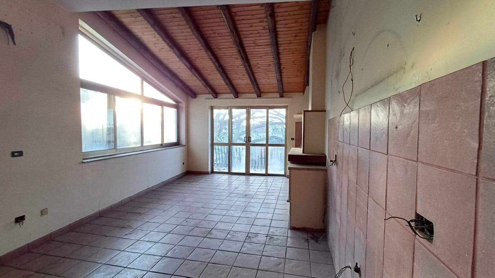 Ampio soggiorno con grandi finestre e tetto in legno, ideale per rinnovare la casa, con luce naturale e spazi luminosi, perfetto per realizzare la zona living dei tuoi sogni.